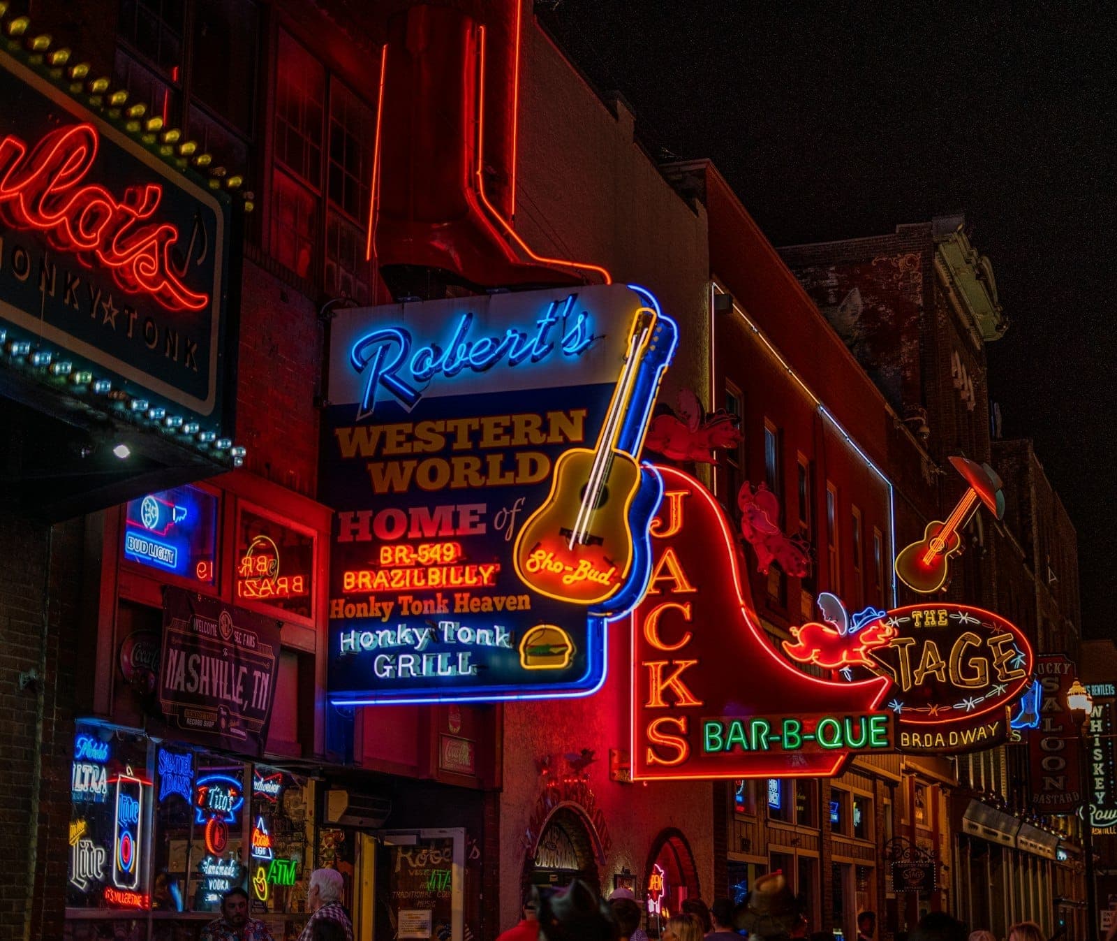 Colorful neon signs for Roberts Western World and Jacks Bar-B-Que light up Nashville’s Music Row at night, attracting visitors to lively honky tonks.