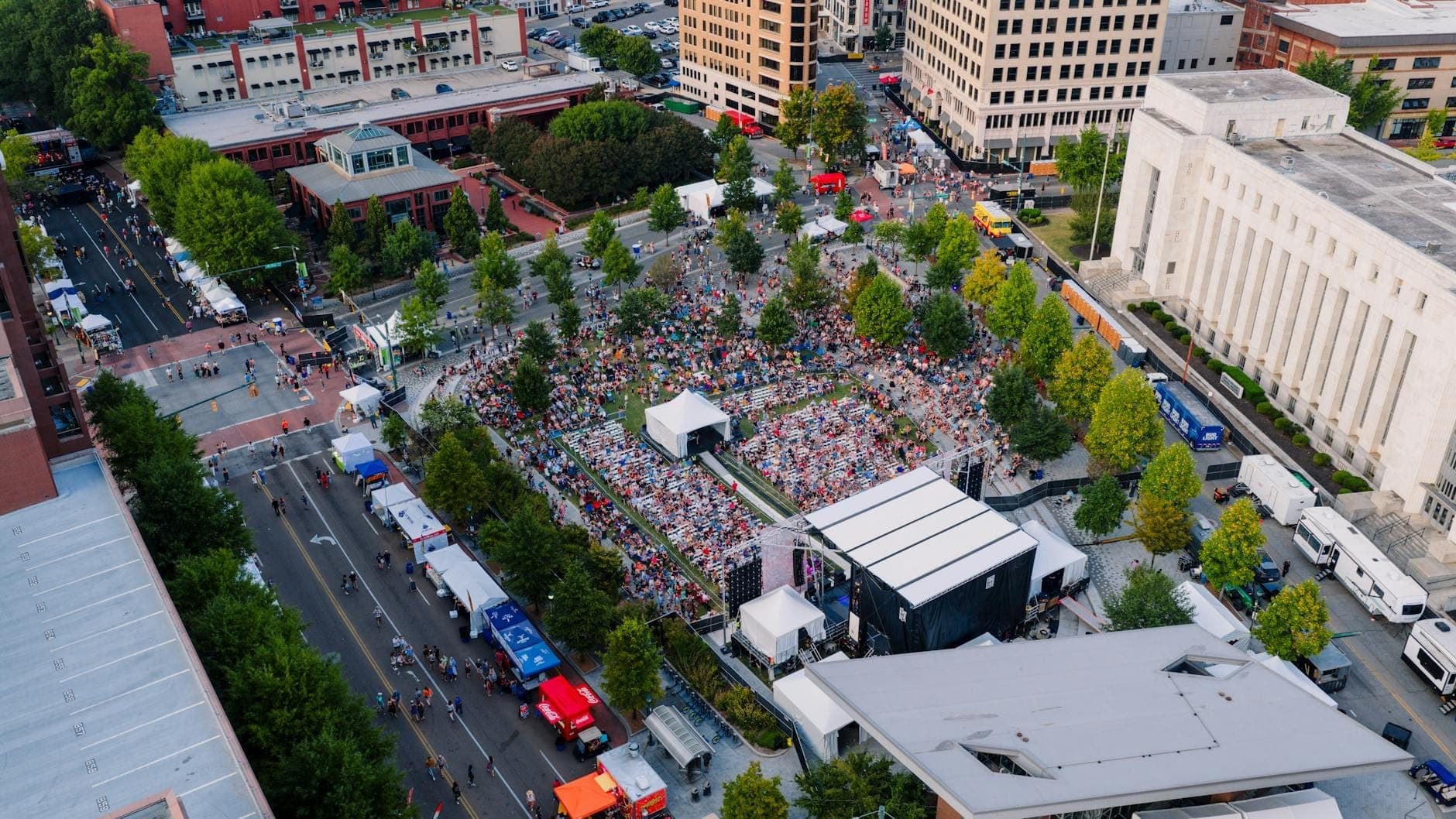 Luftaufnahme einer Outdoor-Veranstaltung in der Innenstadt von Nashville mit dichten Menschenmassen, Food Trucks und umliegenden Gebäuden an einem sonnigen Tag.