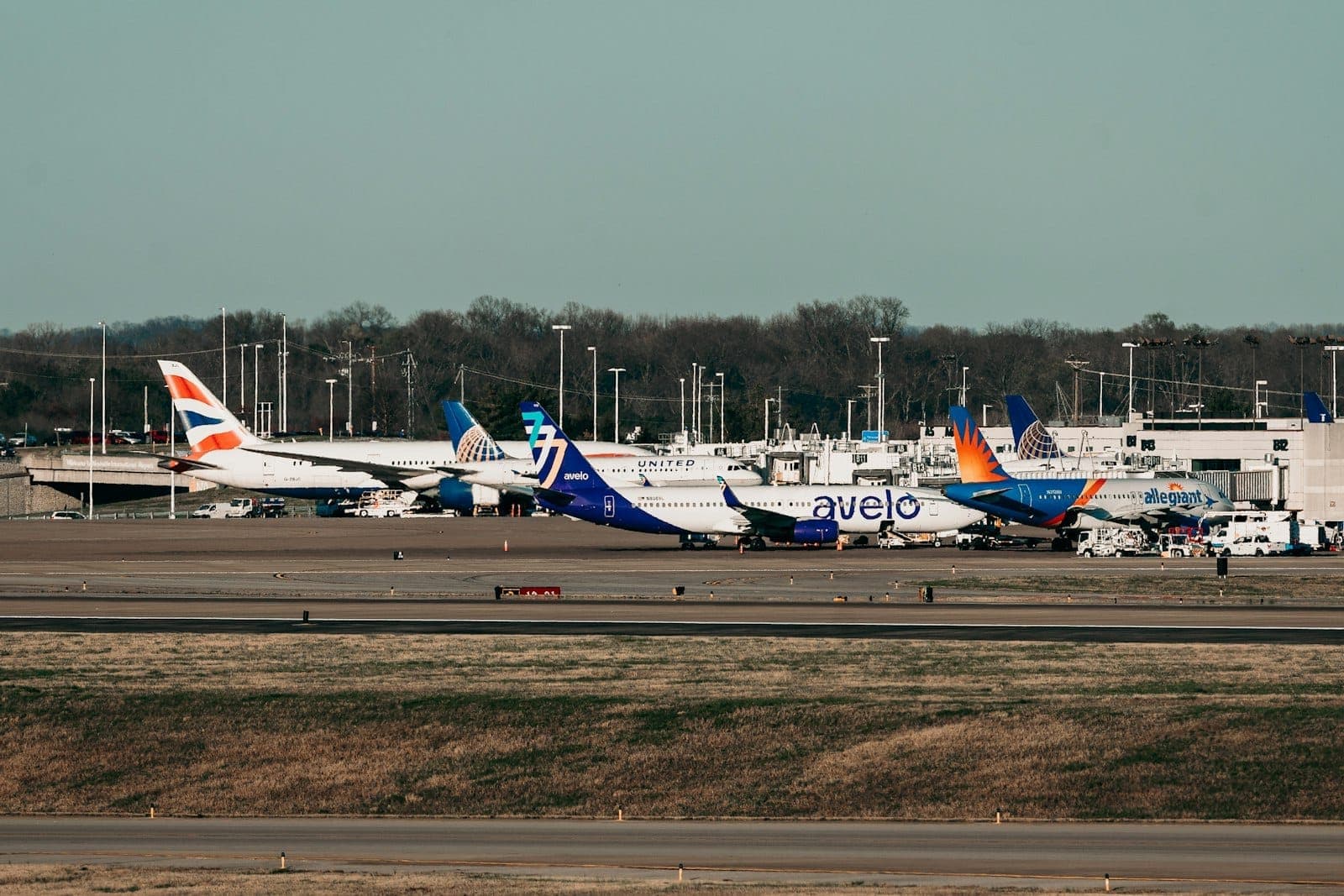 Several commercial airplanes from different airlines are parked at gates outside the terminal at Nashville International Airport on a clear day.