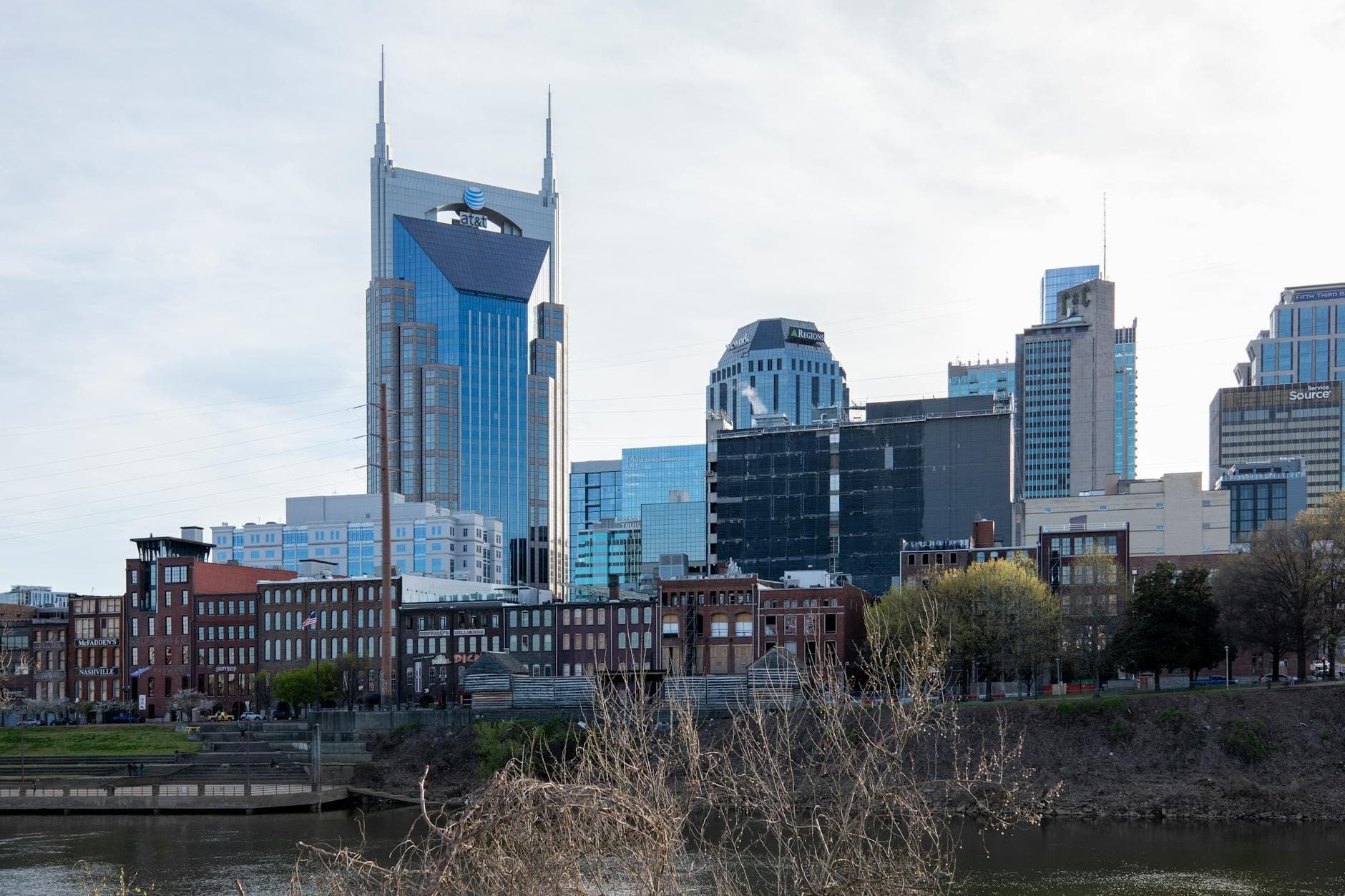 Dzienny widok na panoramę Nashville z ikonicznym budynkiem AT&T, nowoczesnymi hotelami i ceglanymi budowlami wzdłuż nabrzeża rzeki.