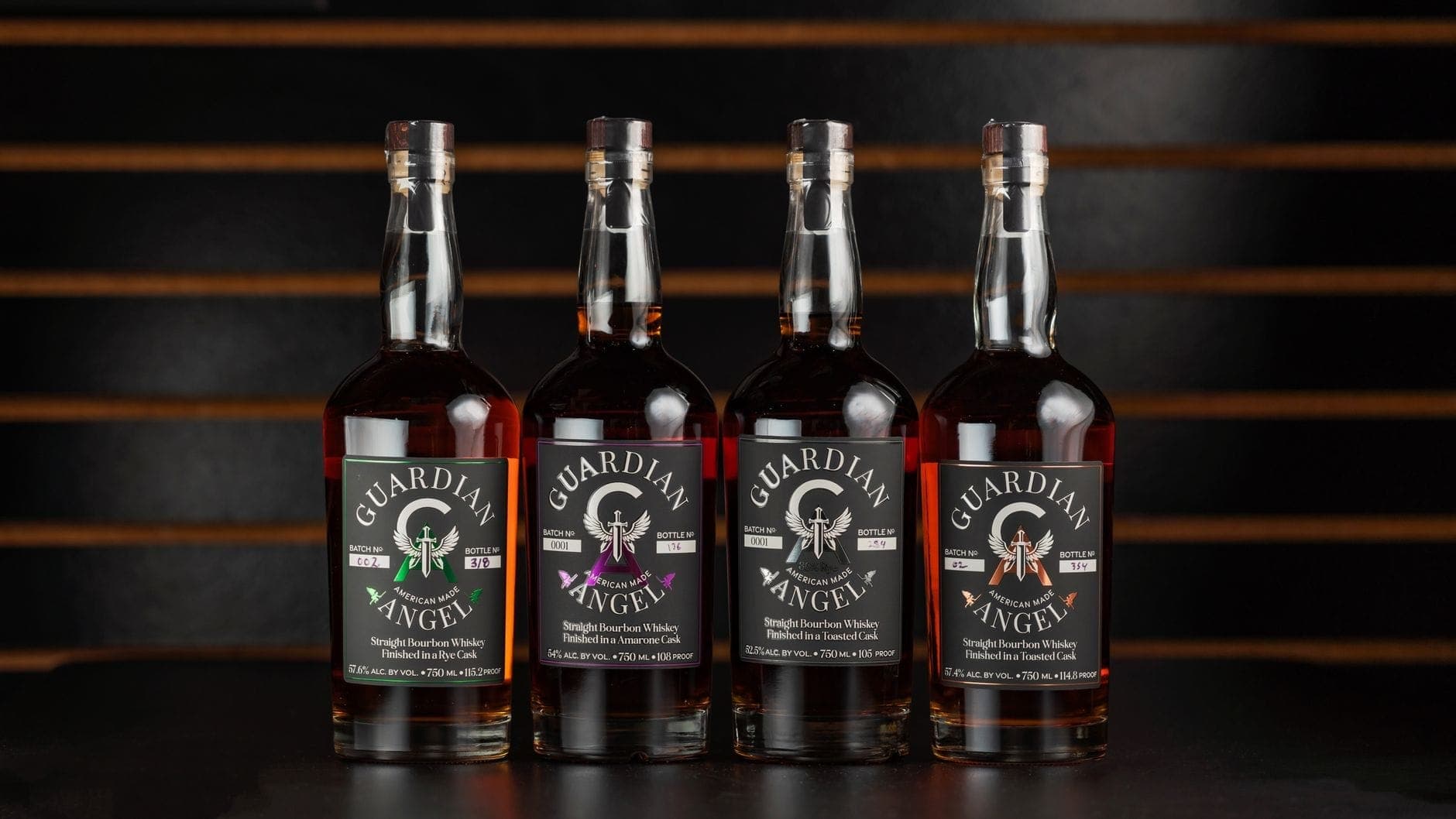 Four bottles of Guardian Angel American whiskey lined up on a bar top with a striped wooden background, captured in a sharp, well-lit landscape photo.