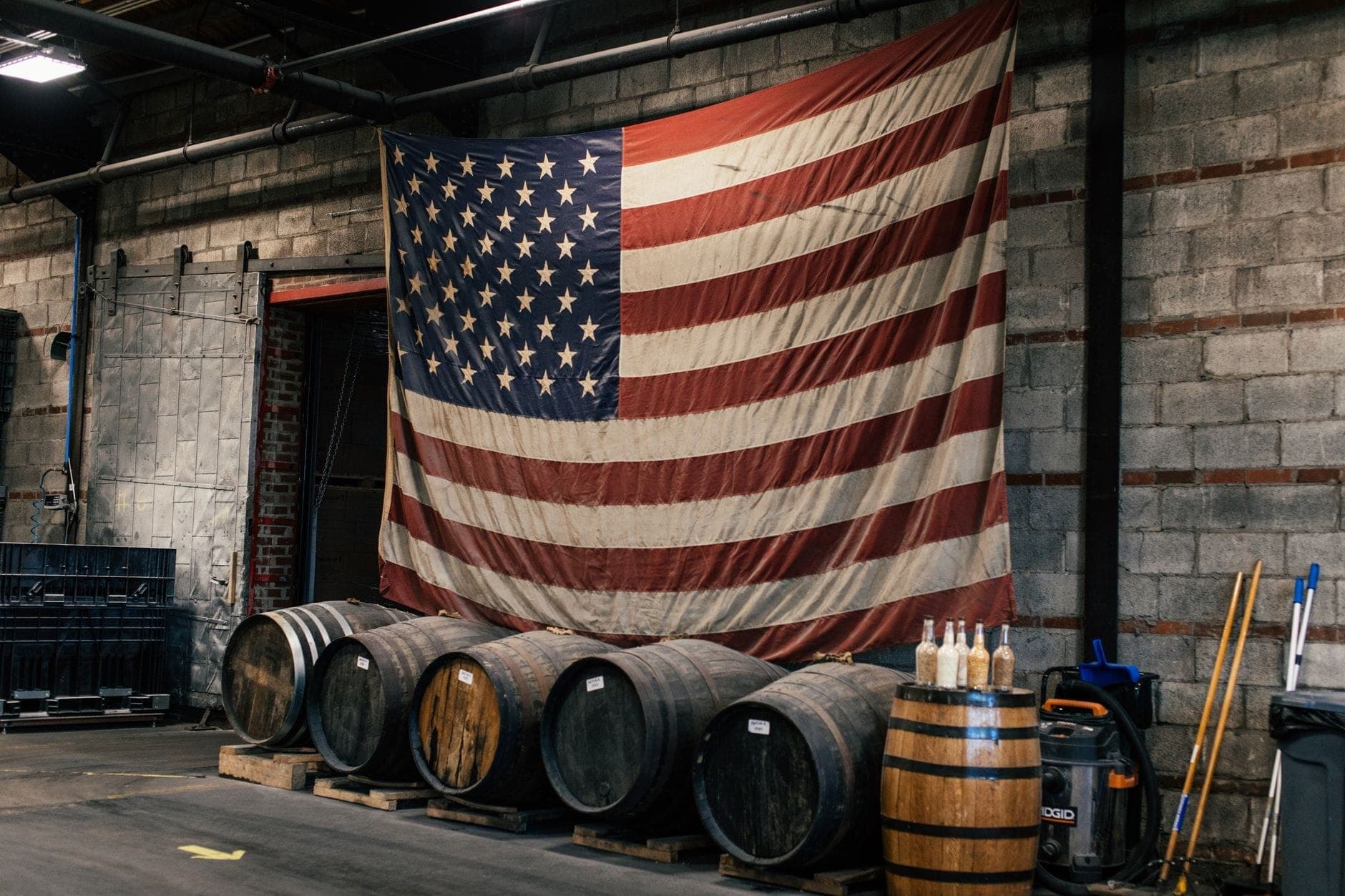 Rząd beczek whiskey wewnątrz miejskiego magazynu gorzelni z dużą amerykańską flagą wiszącą na ceglanej ścianie.