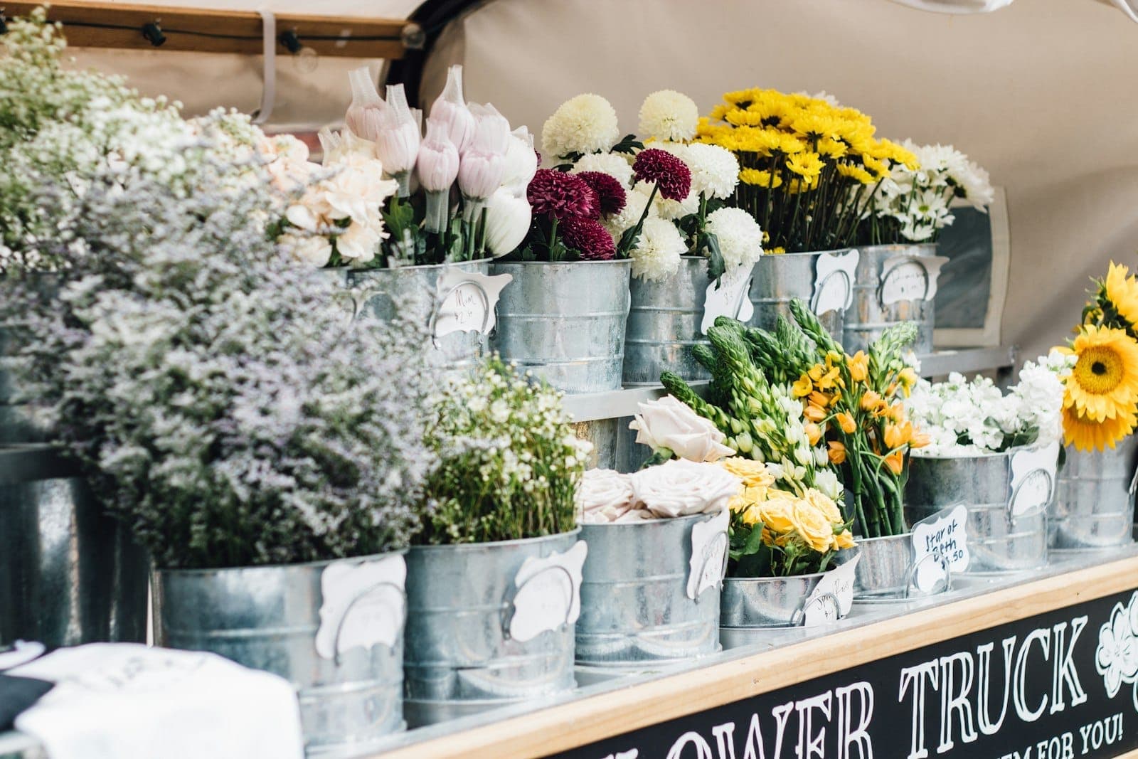 Buckets of colorful fresh flowers arranged on a market stall at an outdoor farmers market, giving a welcoming and vibrant feel.