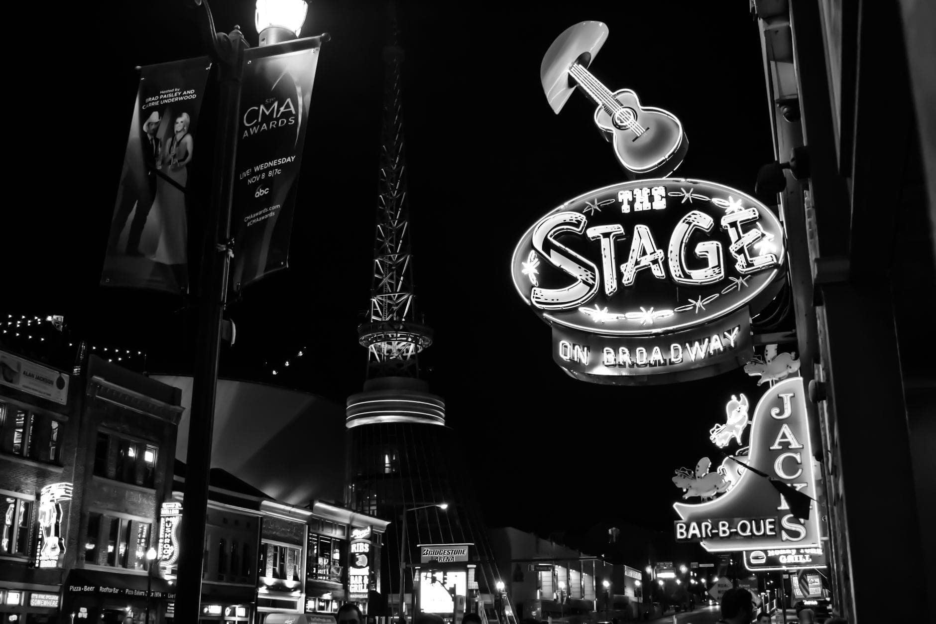 Schwarzweißfoto der Nashville Broadway bei Nacht, mit dem Neonschild des Live-Musik-Lokals The Stage und den Stadtlichtern.