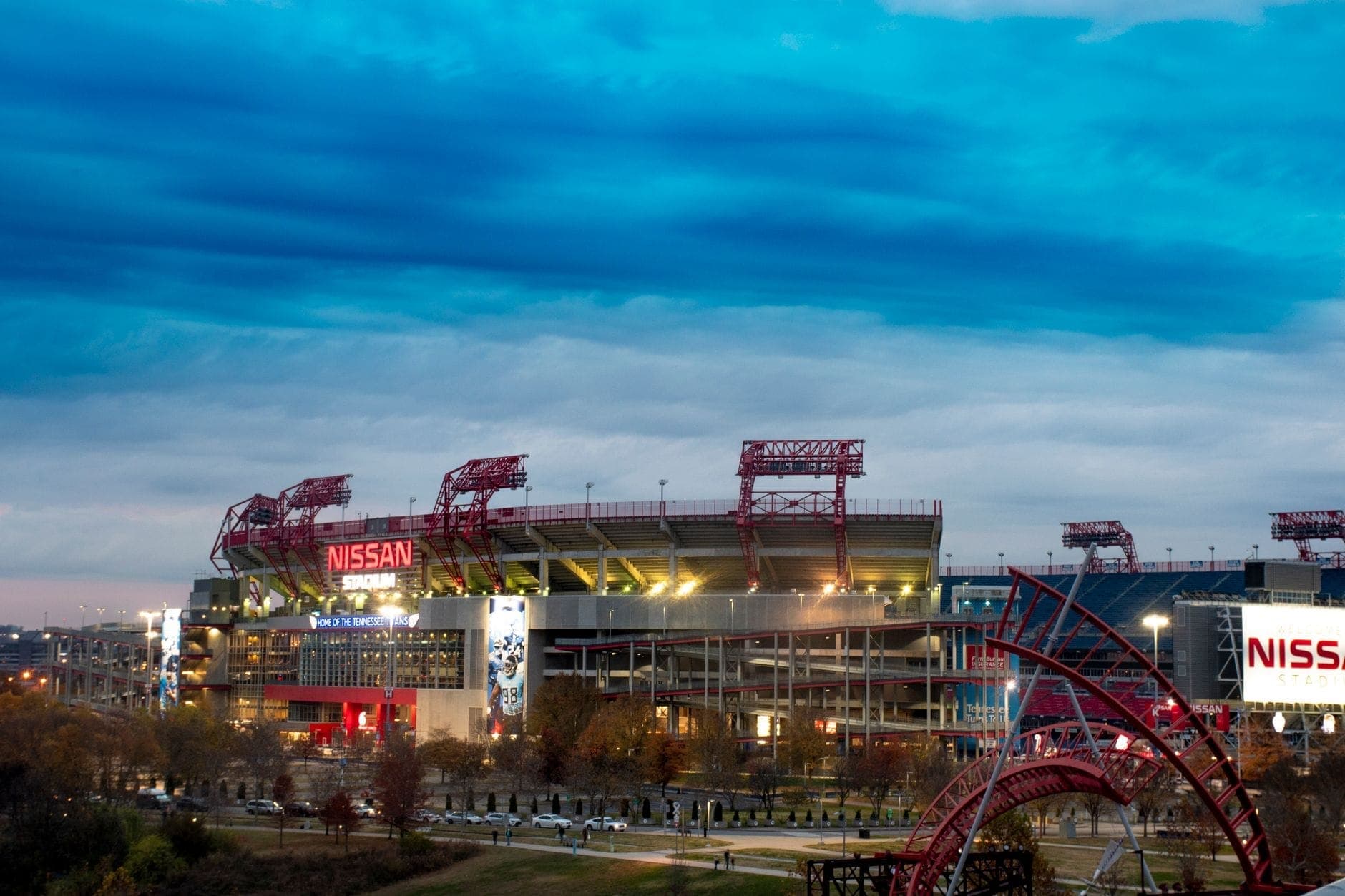 Szeroki widok na Nissan Stadium w Nashville pod nastrojowym wieczornym niebem, z jasnymi światłami stadionu i widoczną infrastrukturą na imprezy plenerowe.