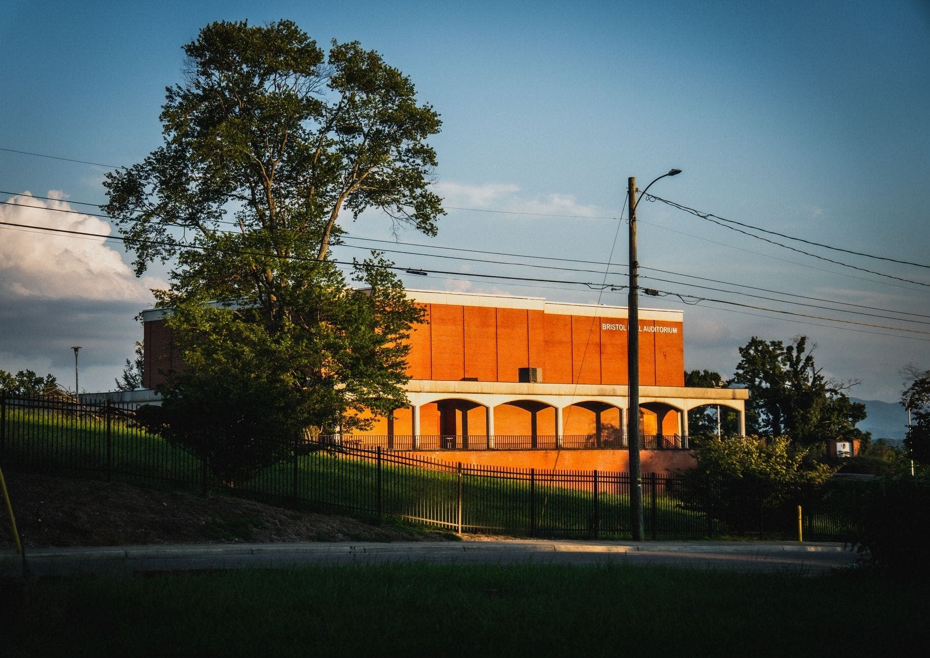Un edificio de ladrillo con 'Grand Ole Opry House' en la fachada, visto desde una zona de césped y árboles con la luz del sol vespertina.
