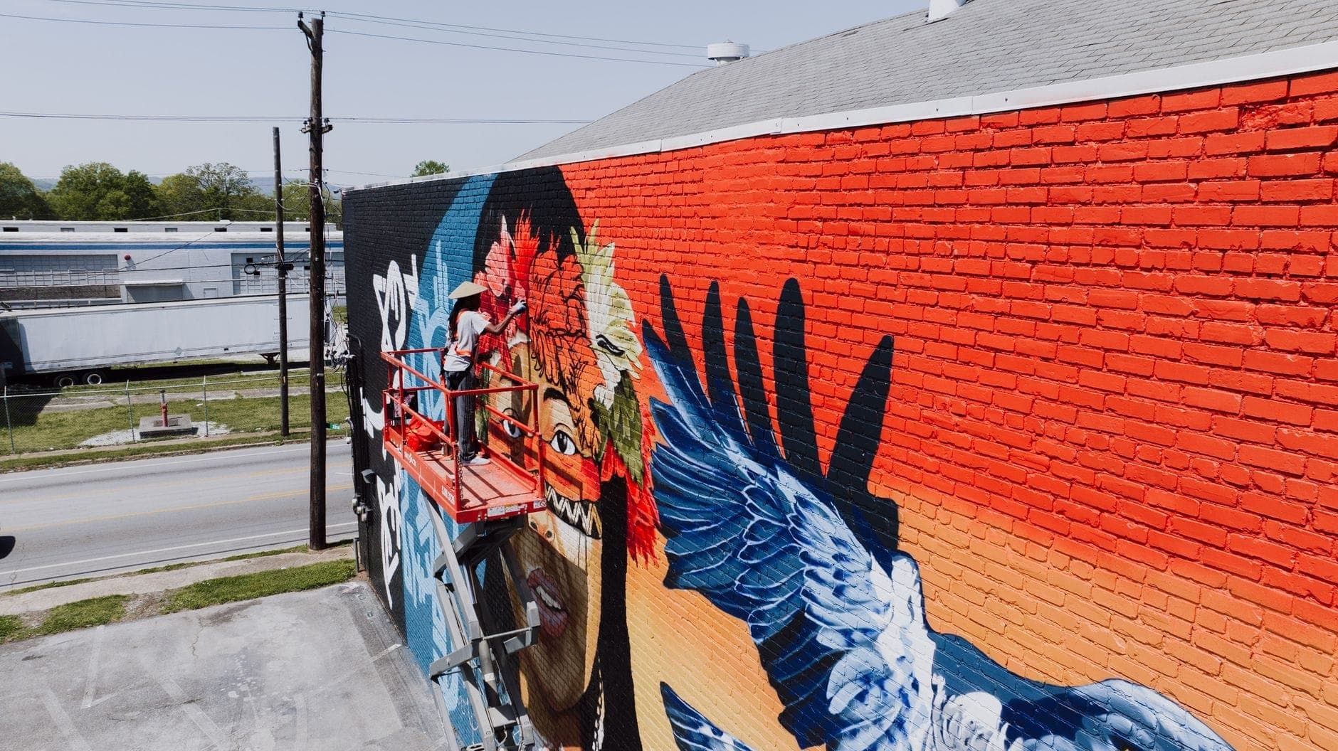Mural brillante en progreso en una pared de ladrillo en Nashville, con una figura cantante de colores, plumas y elementos dinámicos azules y rojos.