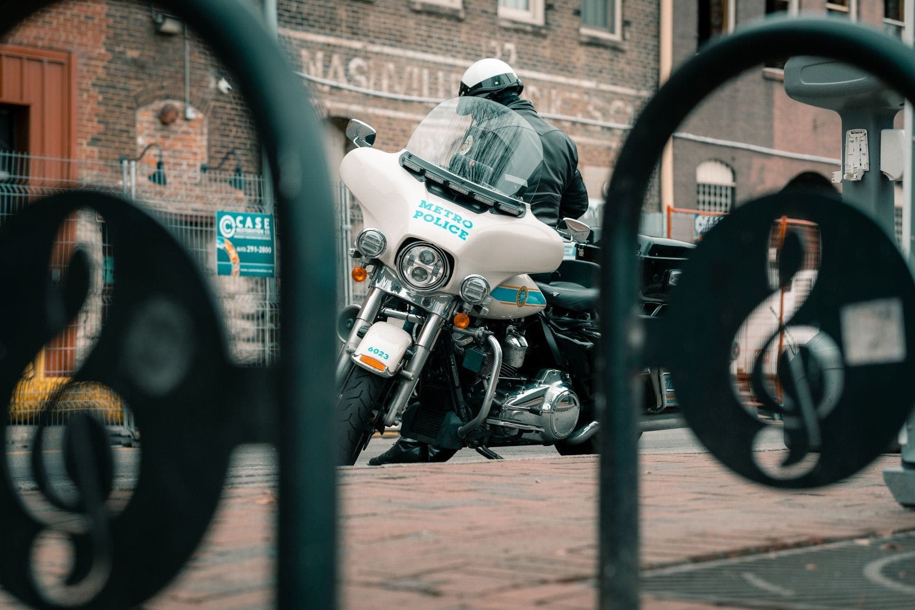 Oficial de policía de Metro Nashville en motocicleta estacionada frente a un edificio de ladrillo, visto a través de una barandilla en forma de nota musical.