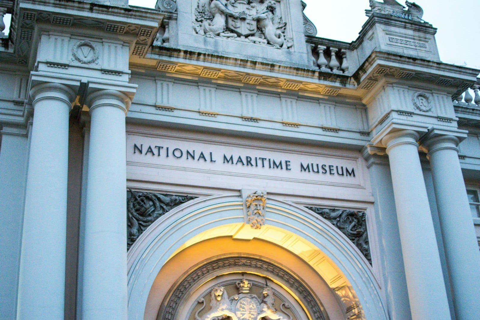 Haupteingang des National Maritime Museum in Greenwich mit imposanten Säulen, Steinmetzarbeiten und abendlicher Beleuchtung.