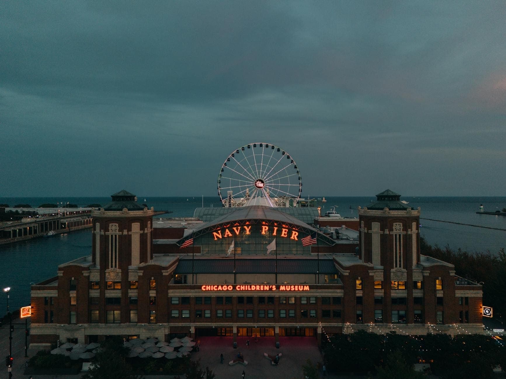 Luftaufnahme des Navy Pier in Chicago in der Abenddämmerung, mit dem beleuchteten Riesenrad und dem Lake Michigan im Hintergrund.