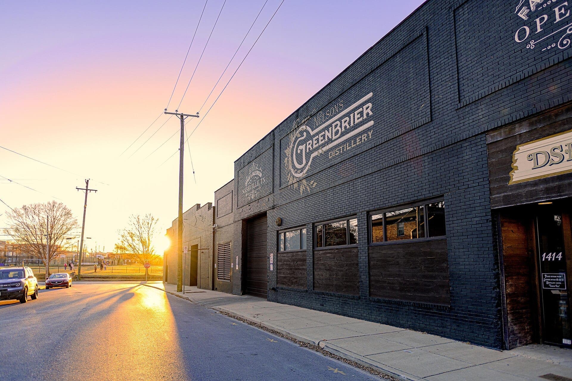 Exterior of Nelson's Green Brier Distillery in Nashville with brick facade, large signage, and glowing sunset lighting on a quiet street.
