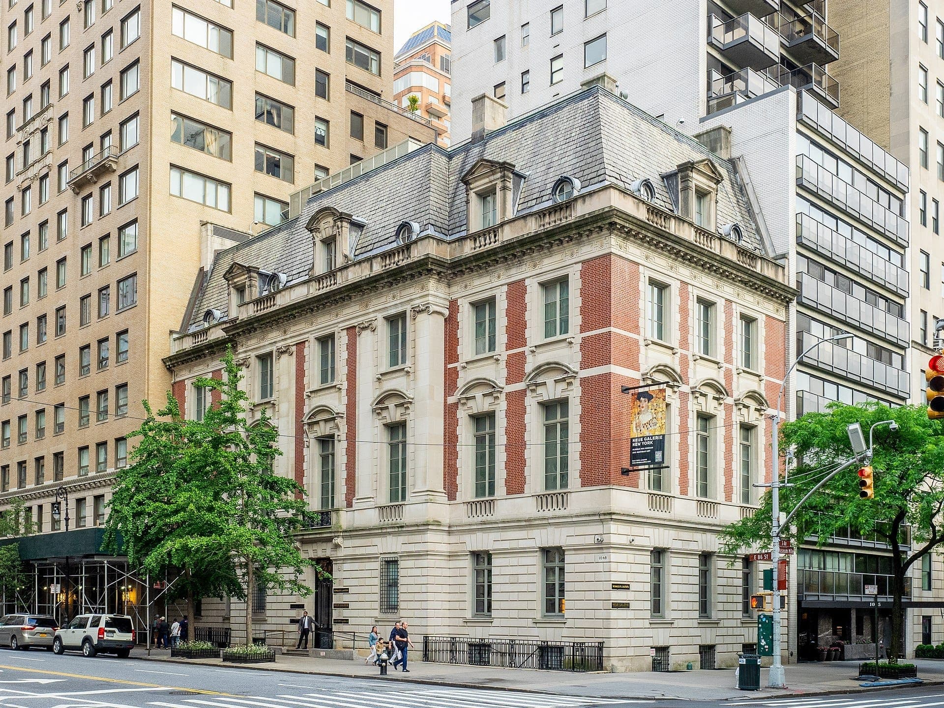 มุมมองภายนอกของ Neue Galerie New York คฤหาสน์ประวัติศาสตร์สไตล์ Beaux-Arts พร้อมด้านหน้าอาคารอิฐแดงและหินบนมุมถนนในเมือง