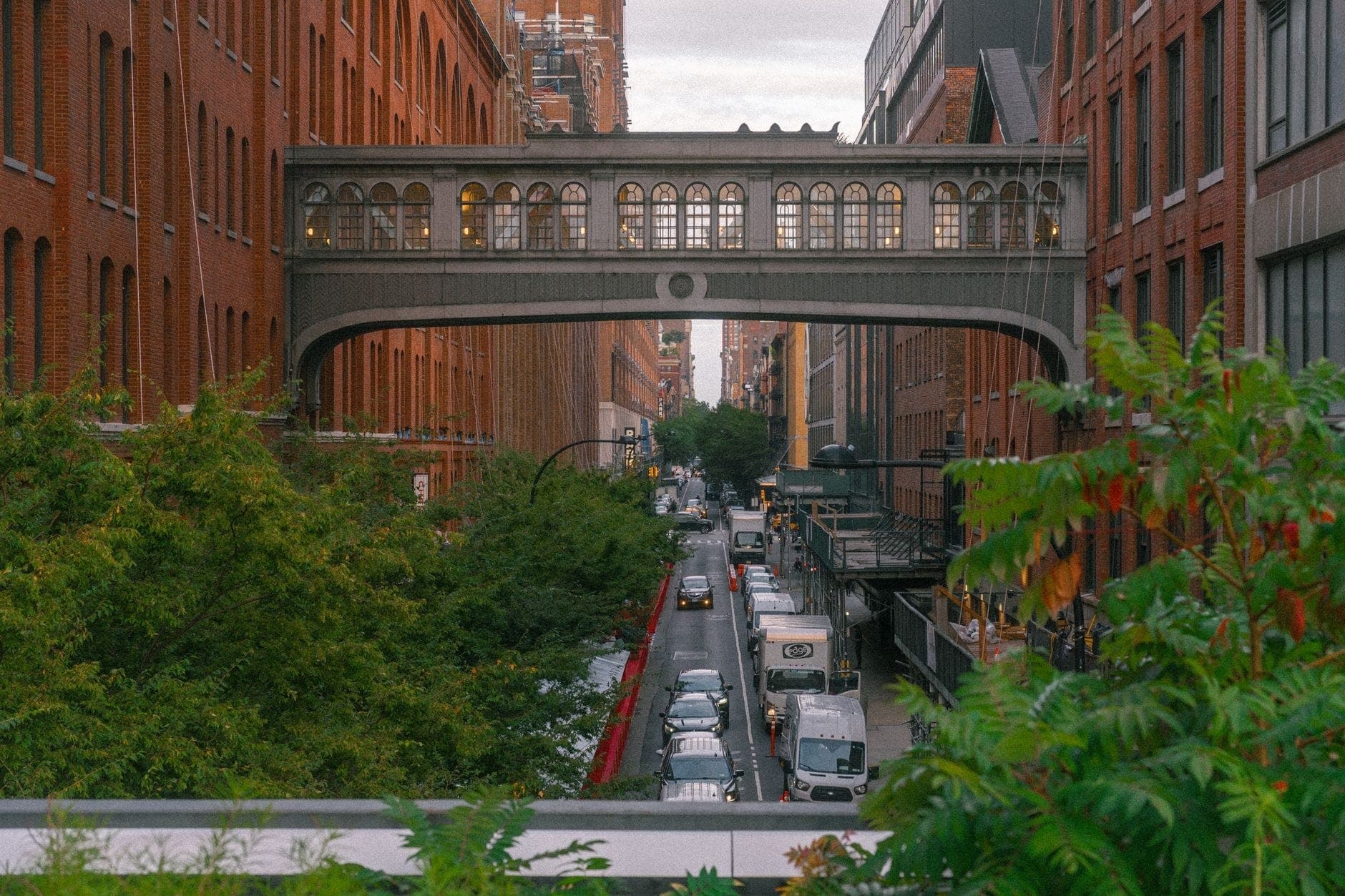 วิวของย่านแกลเลอรี Chelsea ใน New York City โดยมีสะพานลอยที่ยกสูงเหนือถนนที่เรียงรายไปด้วยอาคารอิฐสีแดง ต้นไม้ และการจราจรที่คับคั่งด้านล่าง