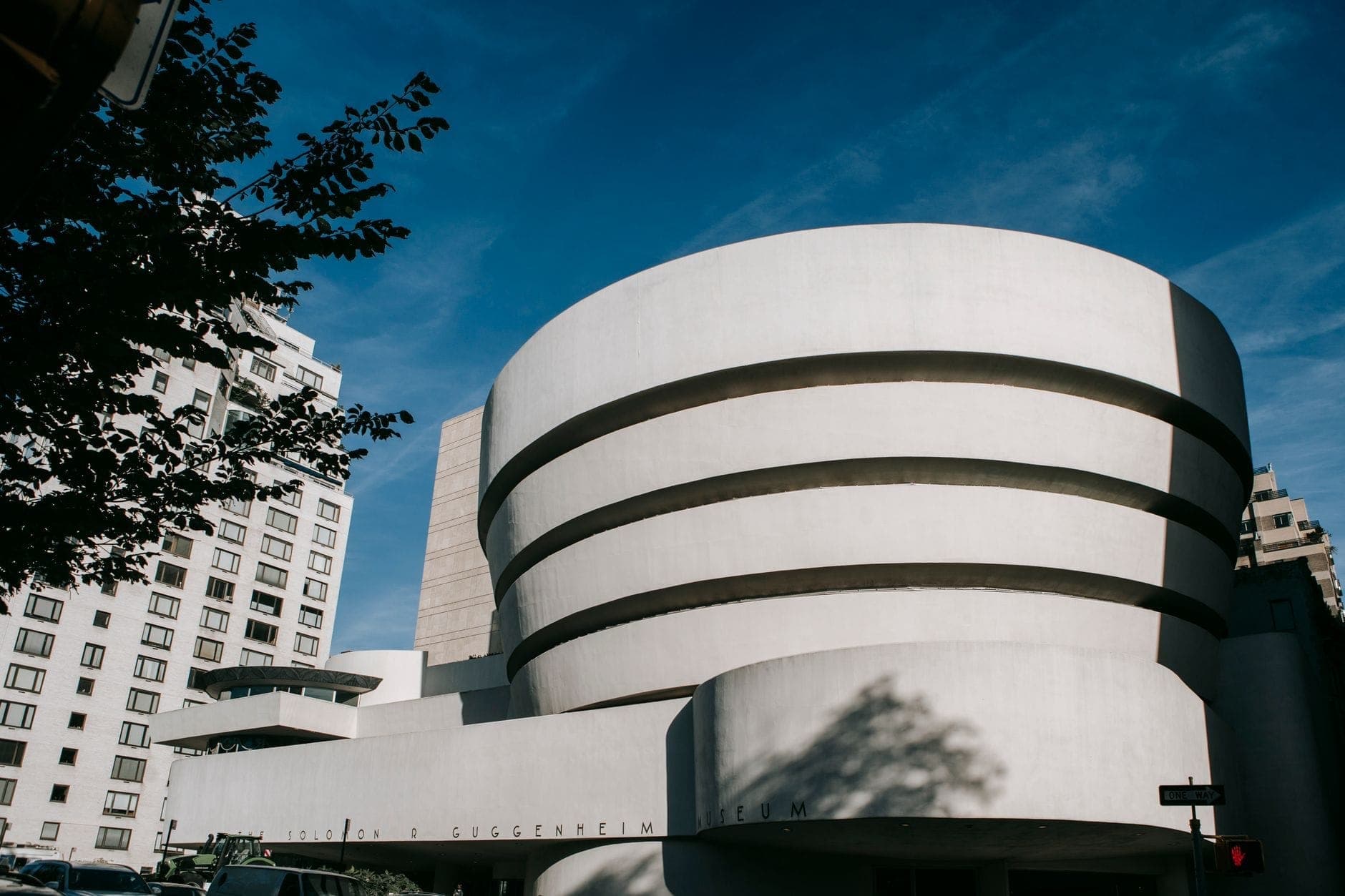 วิวภายนอกของผนังด้านหน้าสีขาวทรงกลมอันเป็นเอกลักษณ์ของ Guggenheim Museum ตัดกับท้องฟ้าสีฟ้าในนิวยอร์กซิตี้พร้อมอาคารโดยรอบ.