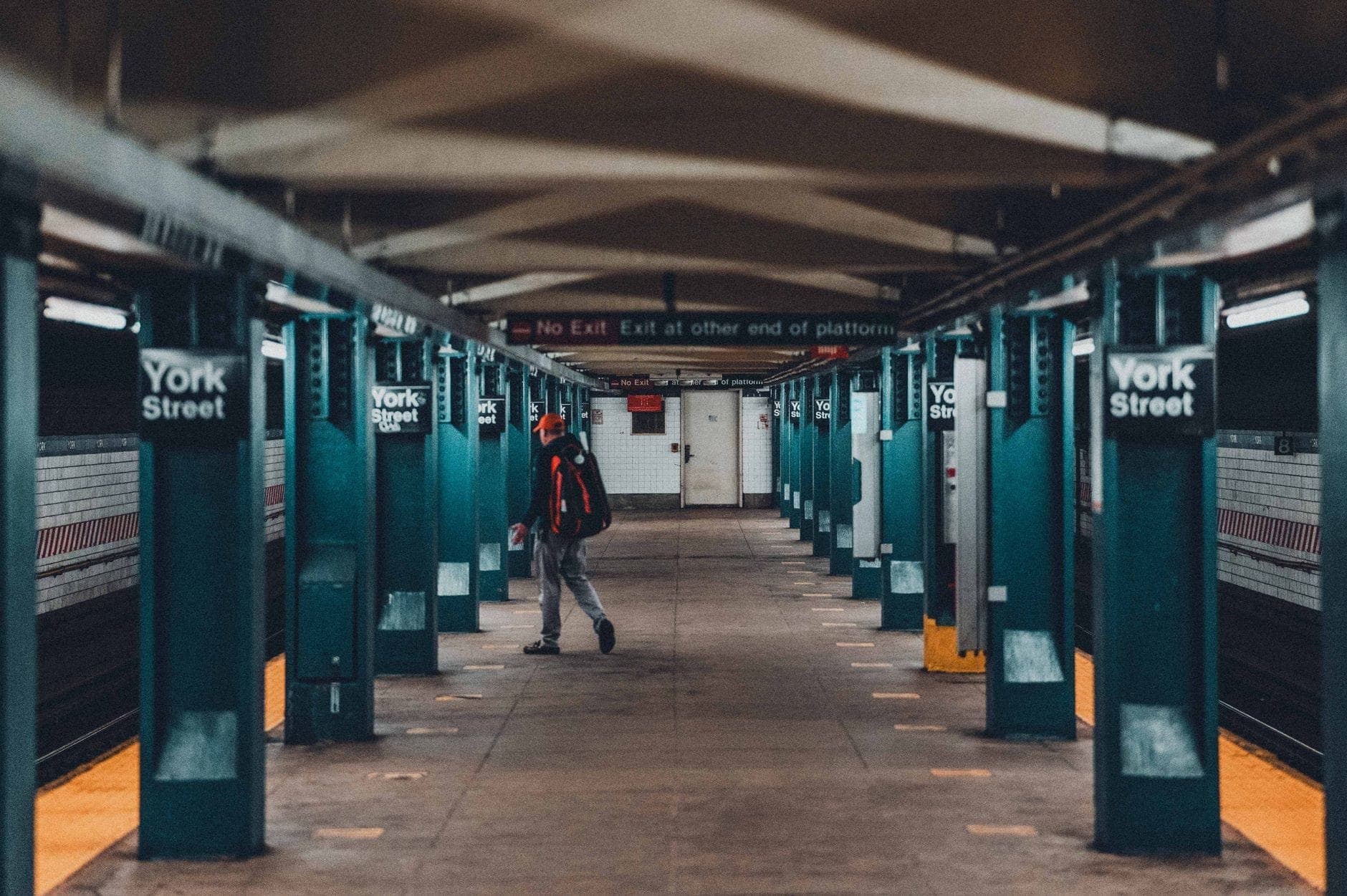 บุคคลกำลังเดินบนชานชาลาของสถานีรถไฟใต้ดิน York Street ในบรูคลิน พร้อมเสาและป้ายที่มองเห็นได้ชัดเจน