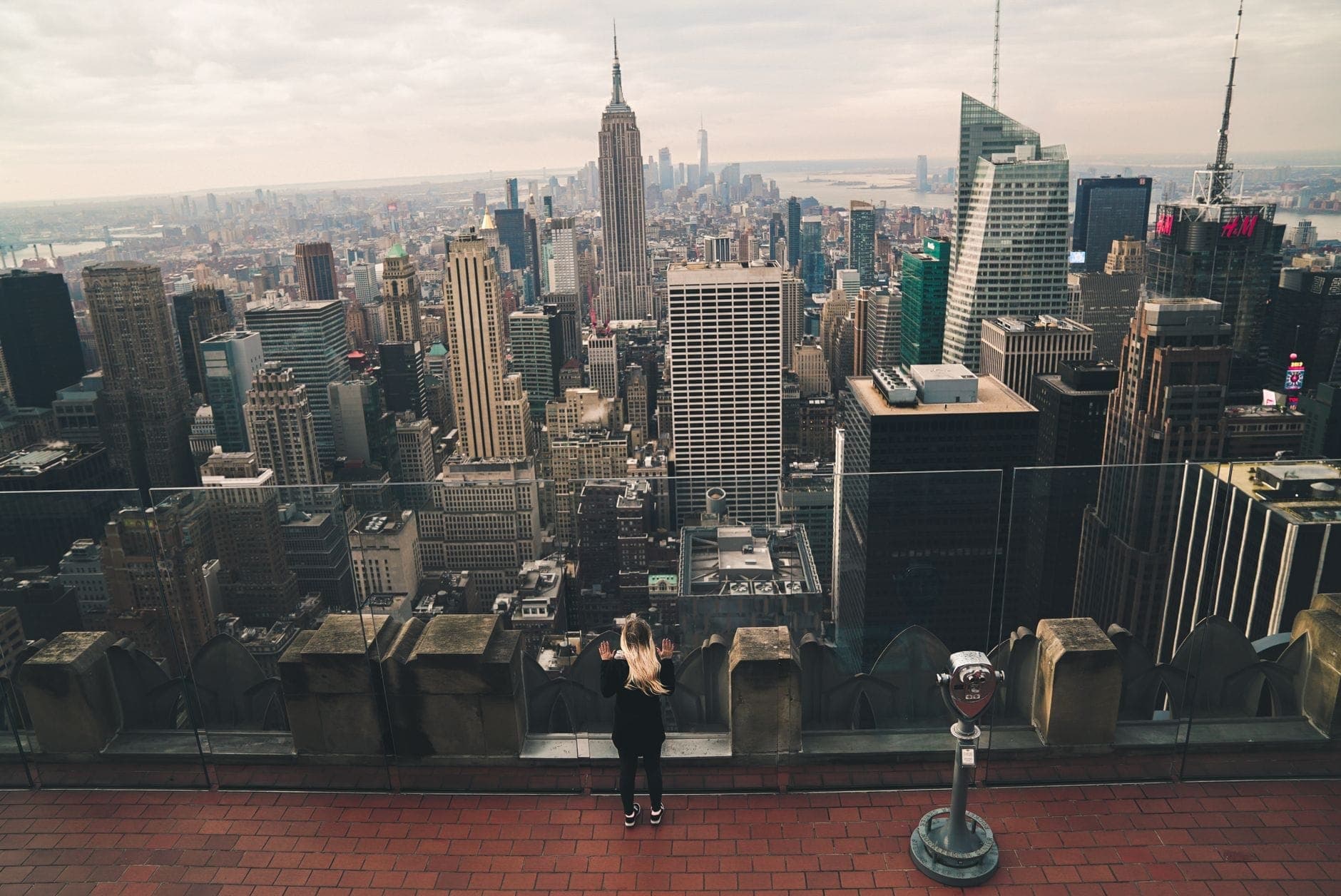 บุคคลมองออกไปจากจุดชมวิว Top of the Rock สู่เส้นขอบฟ้าของนิวยอร์กซิตี้ โดยมี Empire State Building อยู่ในมุมมอง