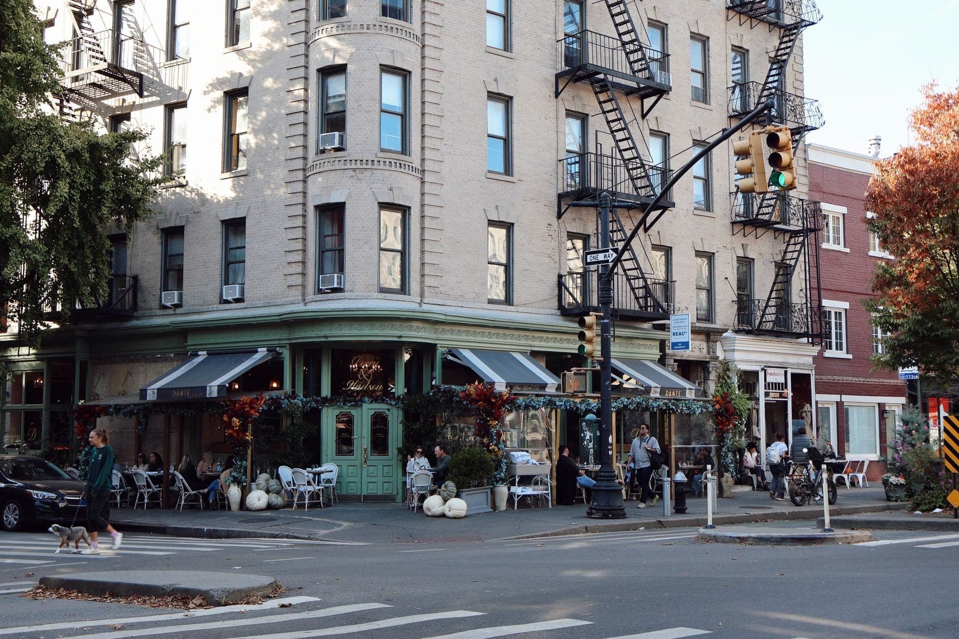 มุมถนนพร้อมคาเฟ่สุดโรแมนติกและที่นั่งกลางแจ้งใน West Village นครนิวยอร์ก ผู้คนรับประทานอาหารใต้การตกแต่งดอกไม้