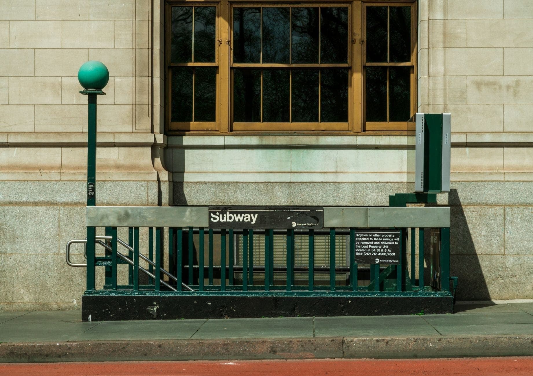 ทางเข้าสถานีรถไฟใต้ดินคลาสสิกของ New York City พร้อมโคมไฟทรงกลมสีเขียว ราวบันได และป้ายรถไฟใต้ดินหน้าอาคารหิน
