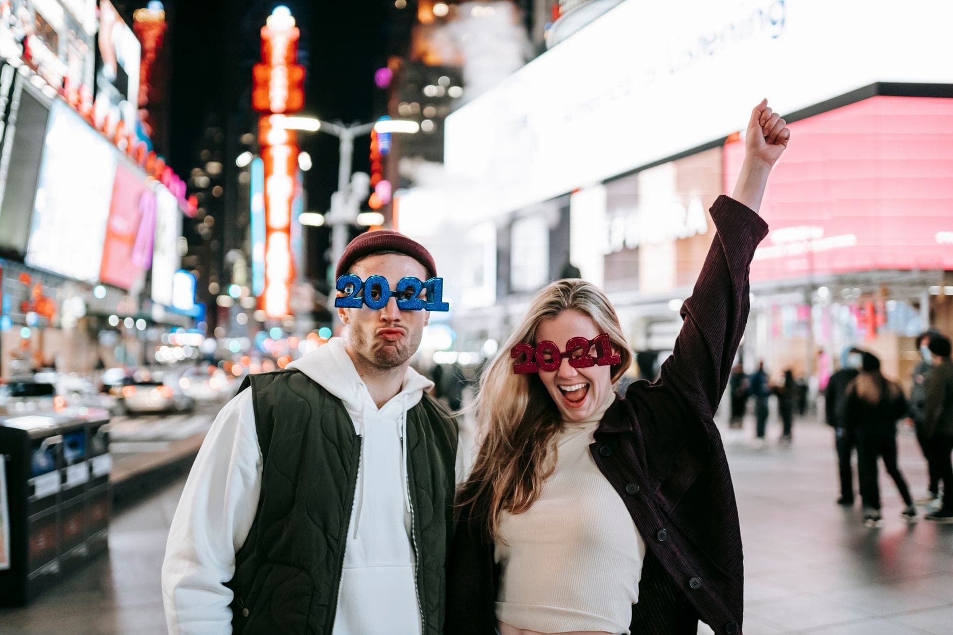 สองคนสวมแว่น 2021 ฉลองในยามค่ำคืนที่ Times Square ล้อมรอบด้วยแสงไฟเมืองและป้ายโฆษณาสว่างไสว