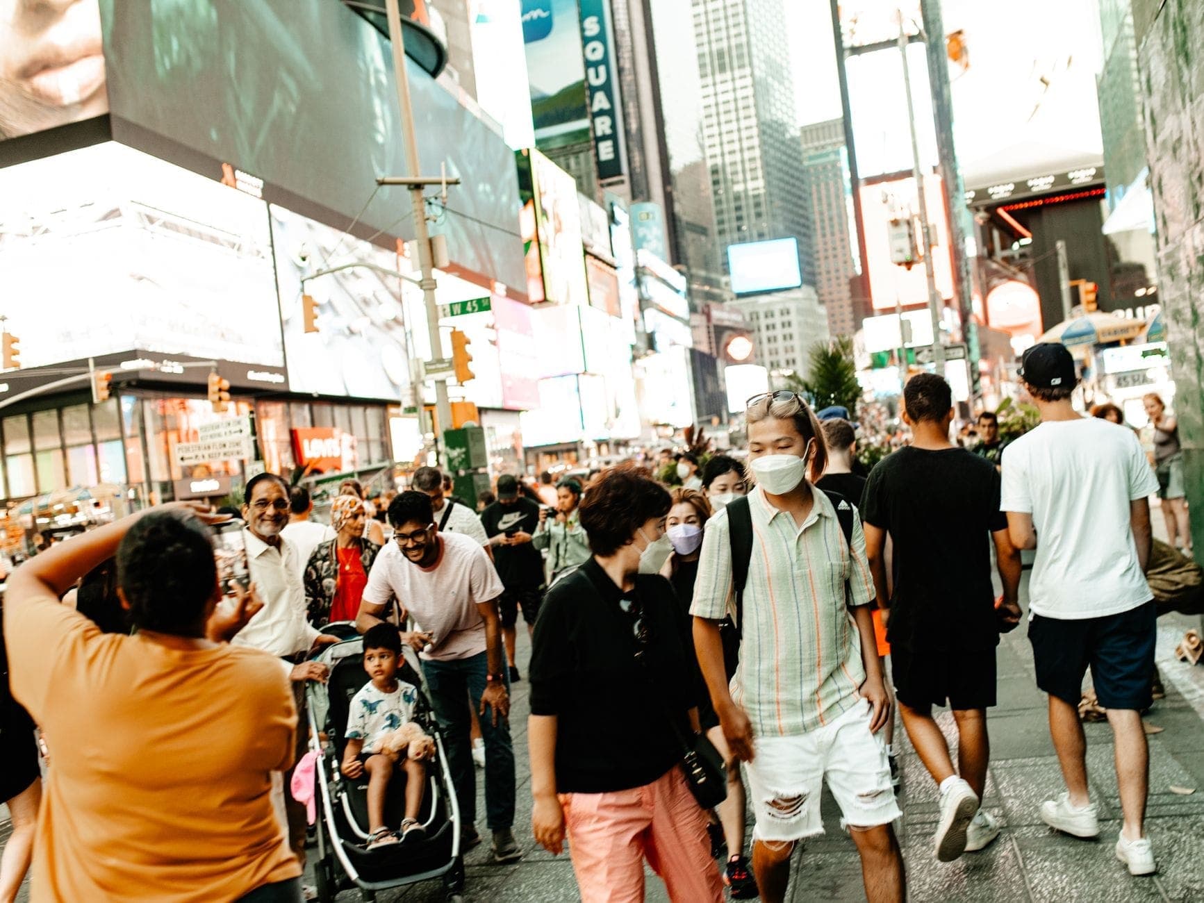 ฝูงชนจำนวนมากกำลังเดินผ่าน Times Square ที่เต็มไปด้วยแสงแดดในนิวยอร์กซิตี้ในวันฤดูร้อน