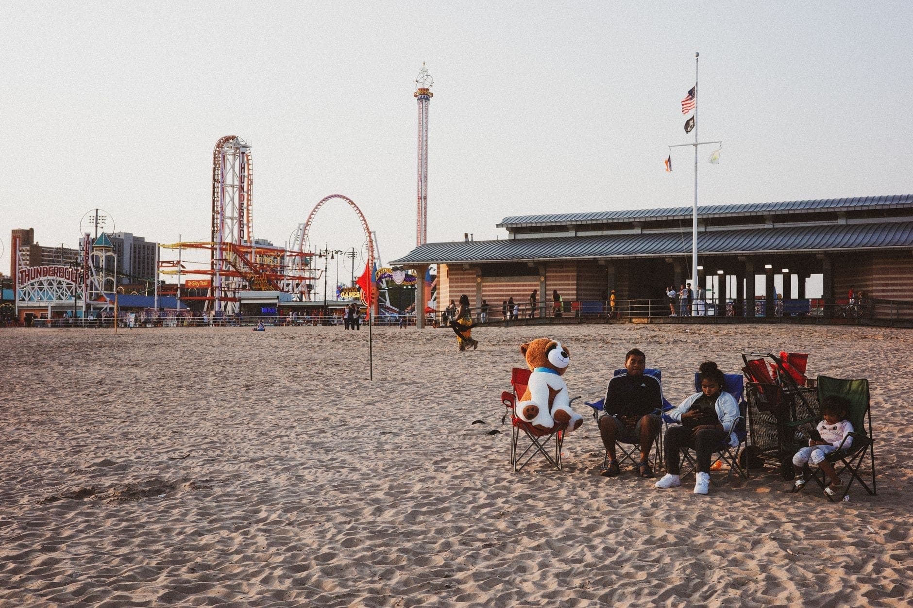 ผู้คนผ่อนคลายบนชายหาดทรายของ Coney Island โดยมีเครื่องเล่นสวนสนุกและอาคาร boardwalk เป็นฉากหลัง นครนิวยอร์ก