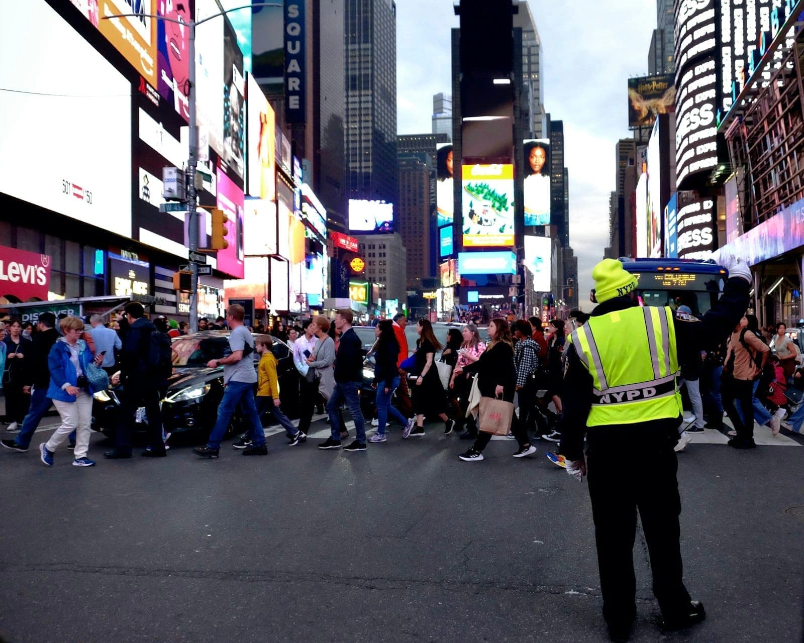 ภาพถนนคึกคักใน Times Square พร้อมเจ้าหน้าที่ NYPD กำลังควบคุมนักท่องเที่ยวจำนวนมากบริเวณทางข้ามถนน ท่ามกลางแสงไฟเมืองที่สว่างไสว