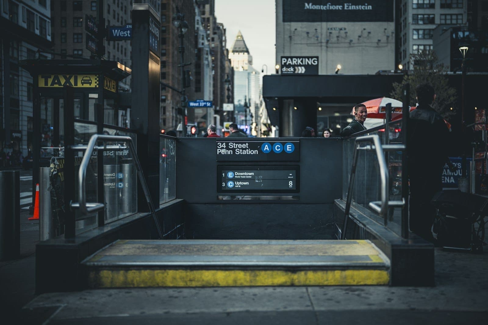 ทางเข้าสถานีรถไฟใต้ดิน Penn Station บนถนน 34th Street พร้อมป้ายรถไฟสาย A, C, E ผู้คน และอาคารในเมืองเป็นฉากหลัง