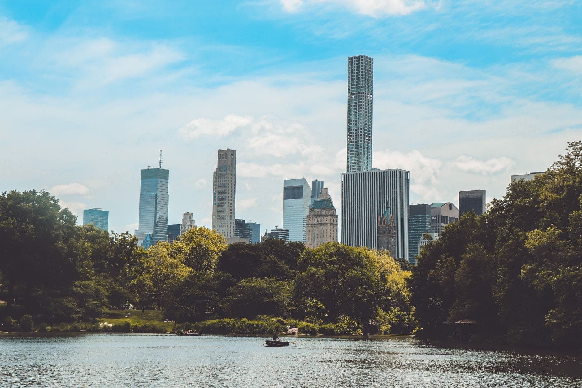 วิวทะเลสาบใน Central Park พร้อมต้นไม้สีเขียวขจีและเส้นขอบฟ้าของ New York City เป็นฉากหลังในวันที่แดดสดใส