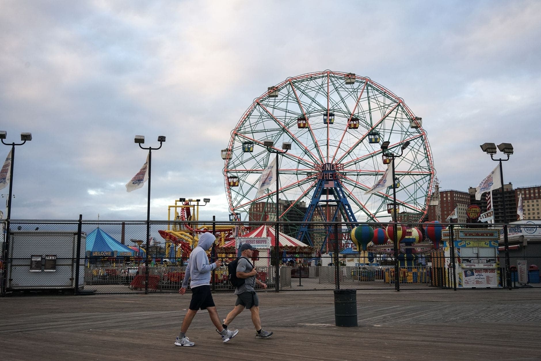 วิวกว้างของทางเดินริมชายหาด Coney Island พร้อมผู้คนที่เดินอยู่ด้านหน้า Wonder Wheel อันโด่งดังและเครื่องเล่นในสวนสนุก