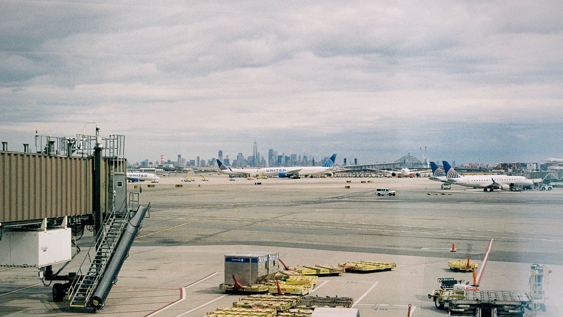วิวลานจอดเครื่องบินที่มีเครื่องบินและเส้นขอบฟ้าของ Manhattan ในระยะไกลภายใต้ท้องฟ้าที่มีเมฆมาก แสดงให้เห็นถึงการจัดการโลจิสติกส์ของสนามบินในสนามบินแห่งหนึ่งใน New York City