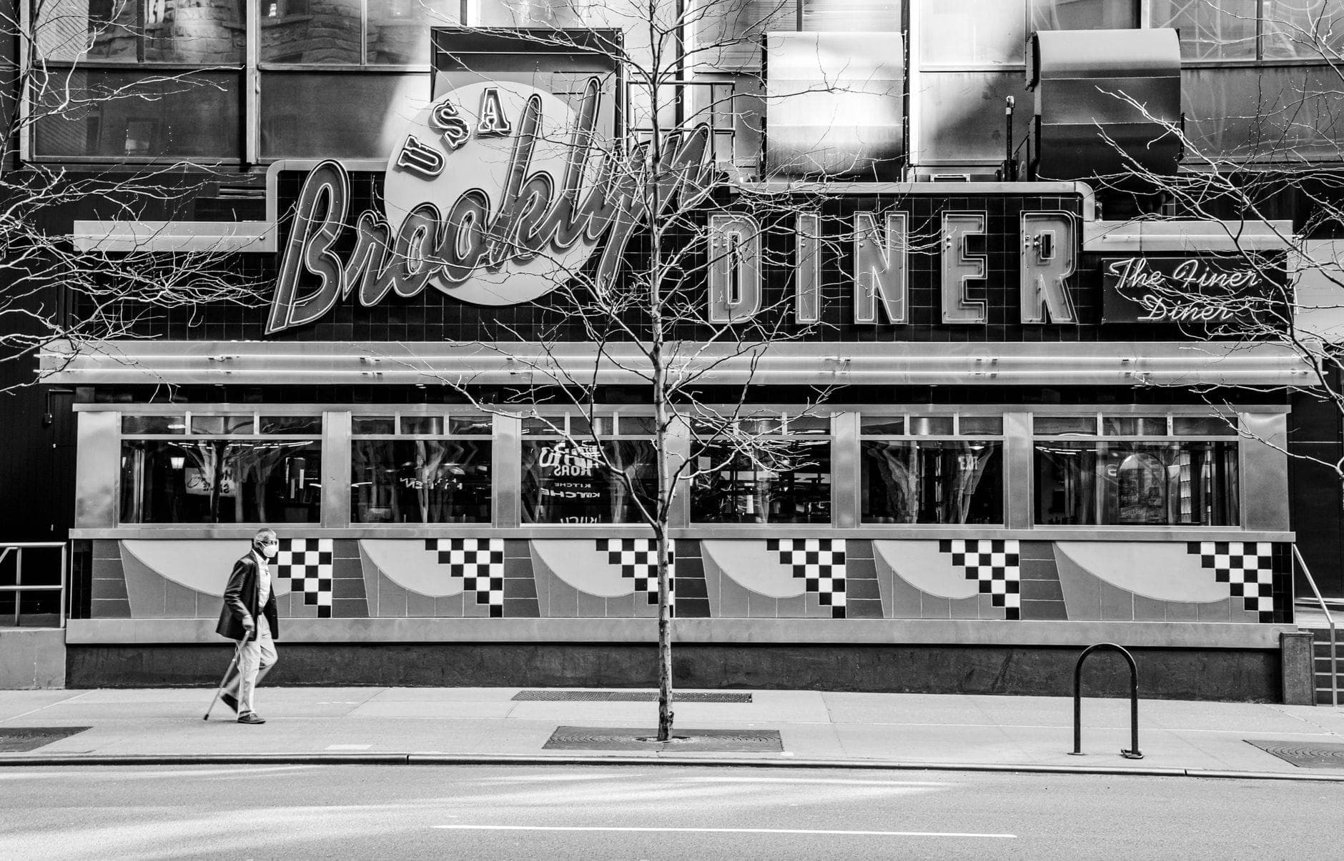 ภาพถ่ายขาวดำของ Brooklyn Diner ในนิวยอร์กซิตี้พร้อมป้ายนีออนและคนเดินถนนที่เดินผ่านทางเข้า