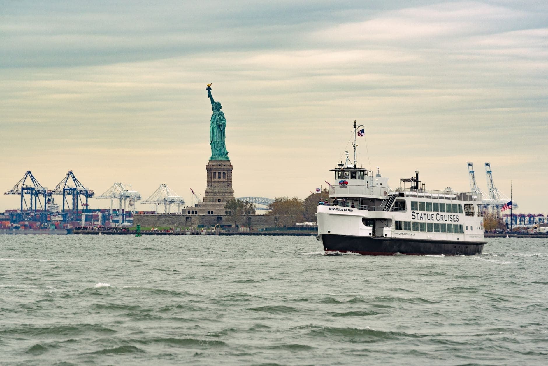 เรือเฟอร์รี่ Statue Cruises มุ่งหน้าสู่ Statue of Liberty โดยมองเห็นรูปปั้นและท่าเรือภายใต้ท้องฟ้ามีเมฆ