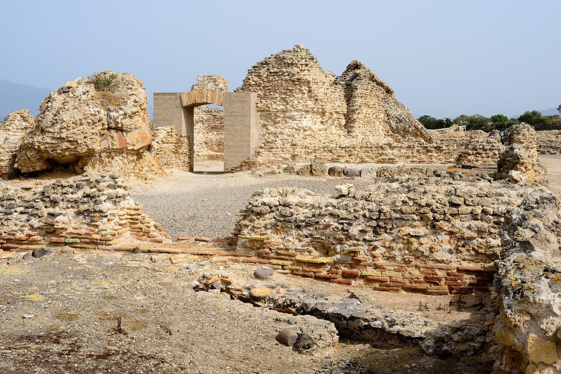 Ruinas de piedra antiguas y muros de ladrillo en el Yacimiento Arqueológico de Nora en Cerdeña bajo un cielo azul despejado.