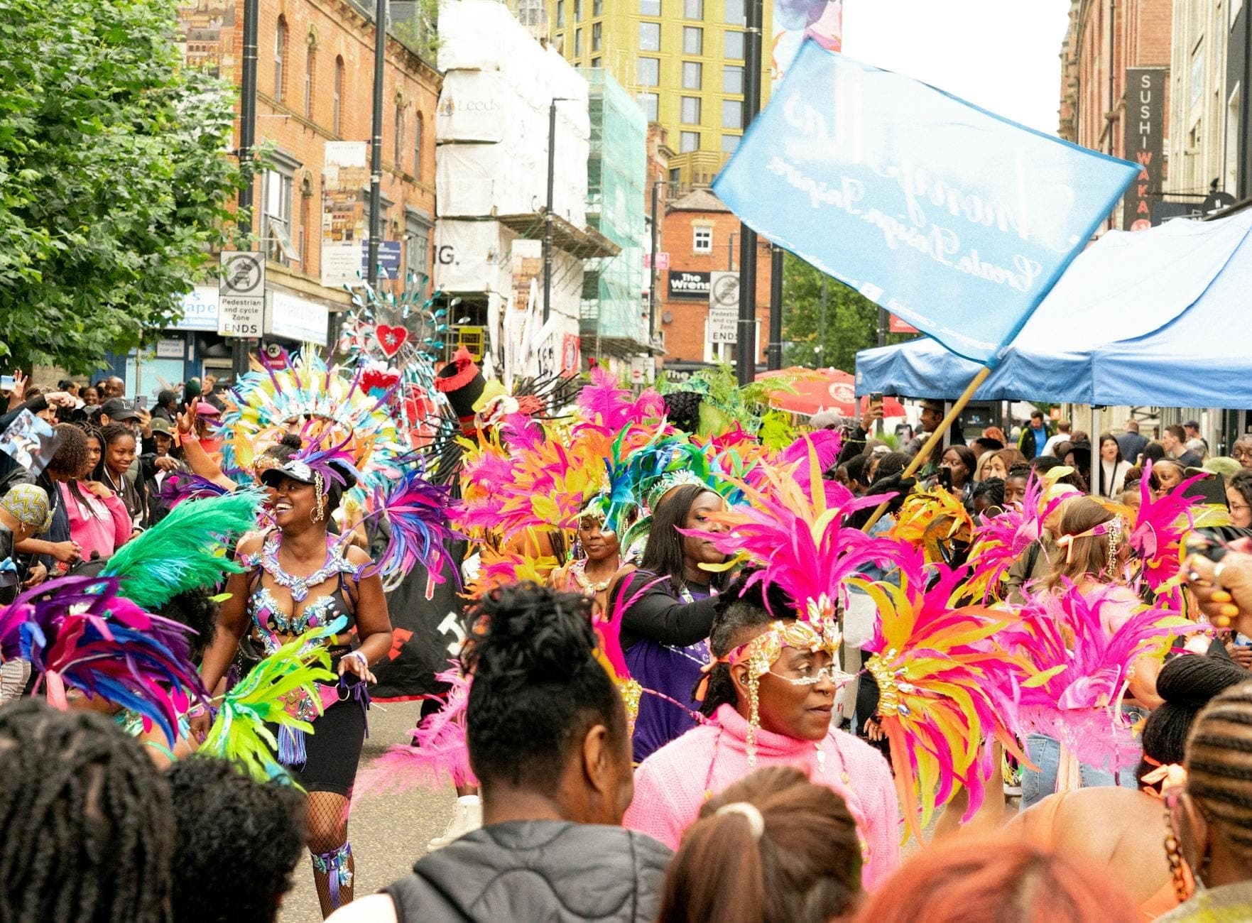 Artistas de desfile con coloridos disfraces y multitudes celebrando al aire libre en una calle de Londres durante un vibrante festival.