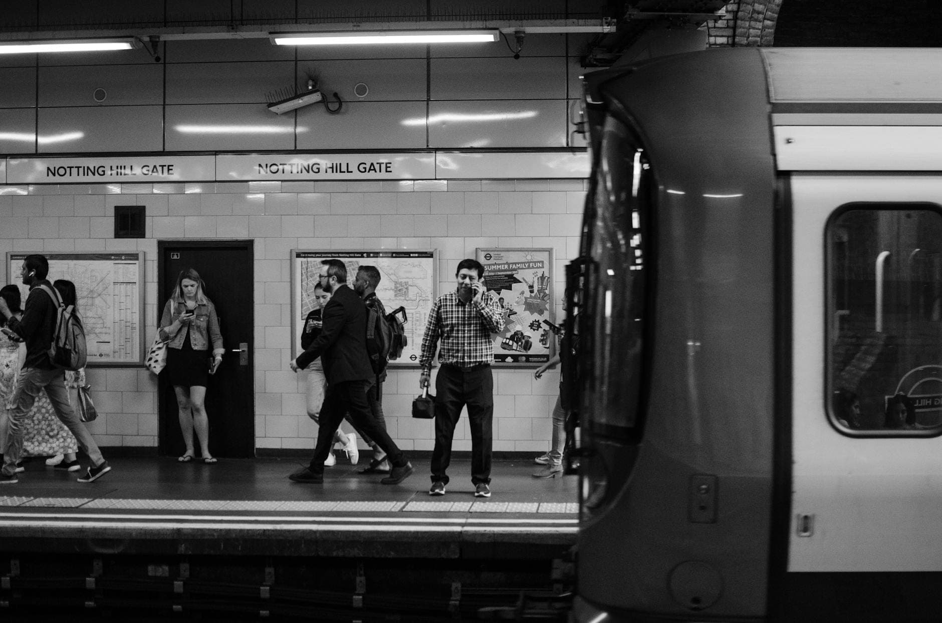 Viajeros de pie y caminando en el andén de la estación de metro Notting Hill Gate de Londres con un tren en primer plano.