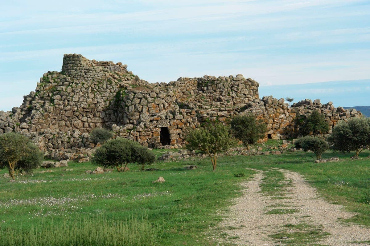 Nuraghe Arrubiu, una enorme fortaleza de piedra antigua, se alza entre hierba verde y arbustos dispersos bajo un cielo azul cerca de Orroli, Cerdeña.