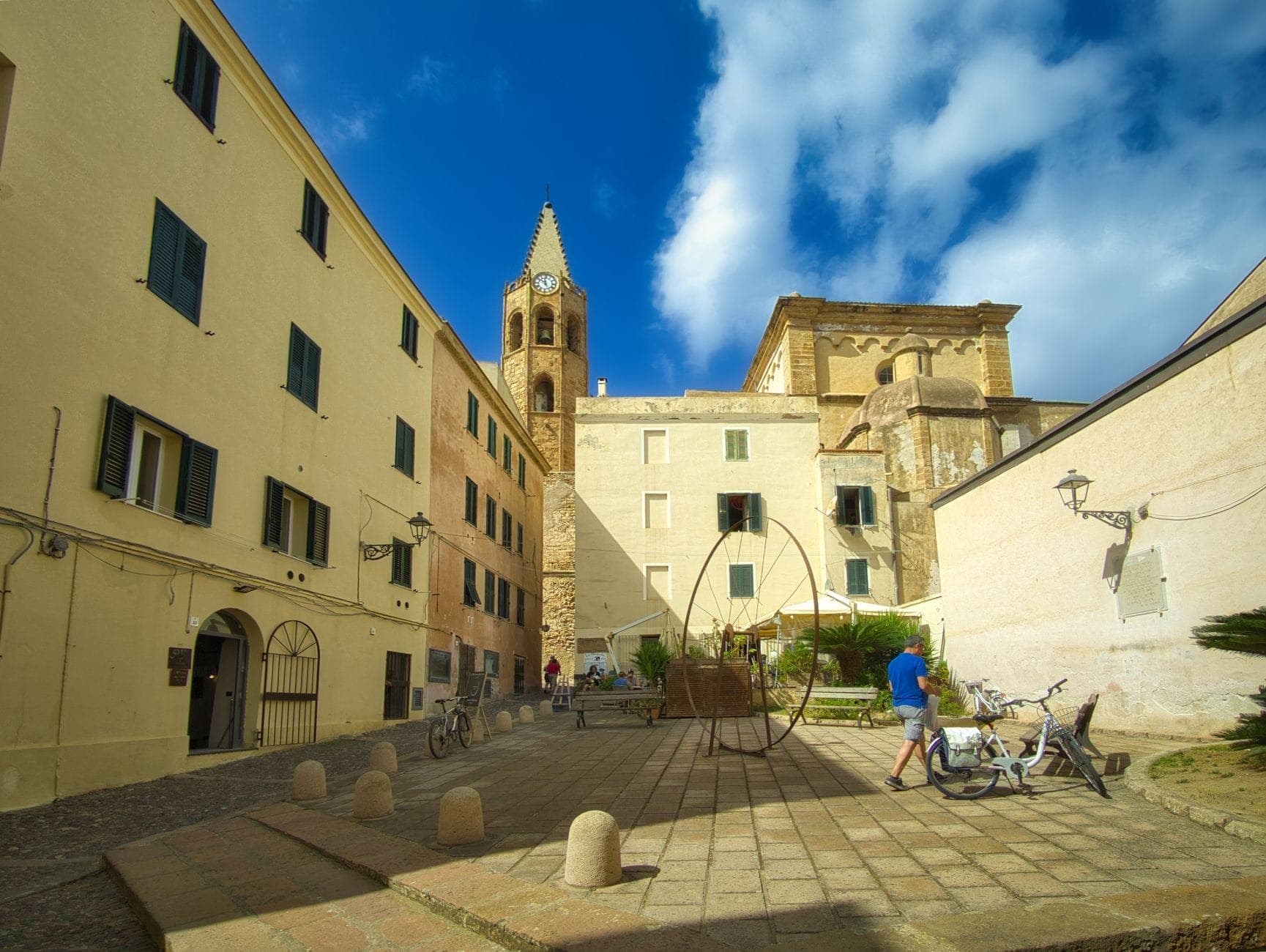 Una iglesia románica con campanario situada en una pequeña plaza, rodeada de edificios históricos en Olbia, Cerdeña.