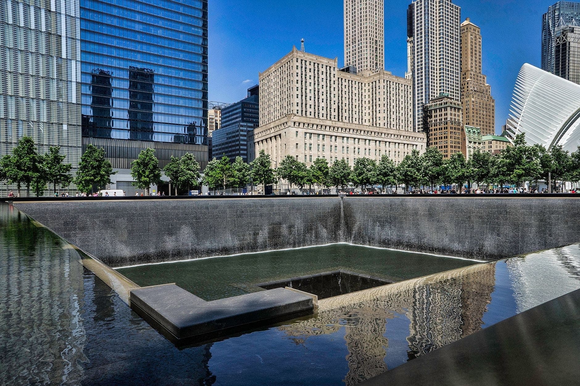สระสะท้อนน้ำของอนุสรณ์สถาน 9/11 ใน Lower Manhattan ล้อมรอบด้วยตึกระฟ้าและ Oculus ในวันที่แดดจ้า