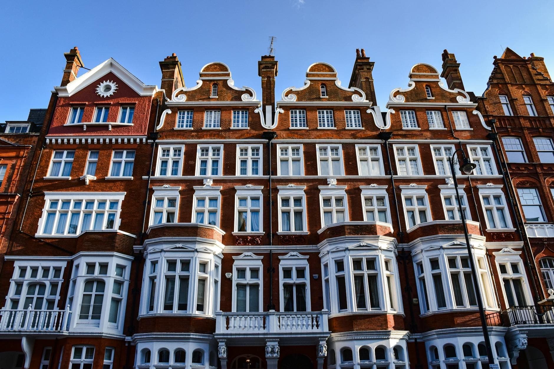 Açık mavi bir gökyüzü altında süslü kırmızı tuğla ve beyaz detaylı Edwardian binaların görkemli sırası — Londra mimarisinin simgesi.