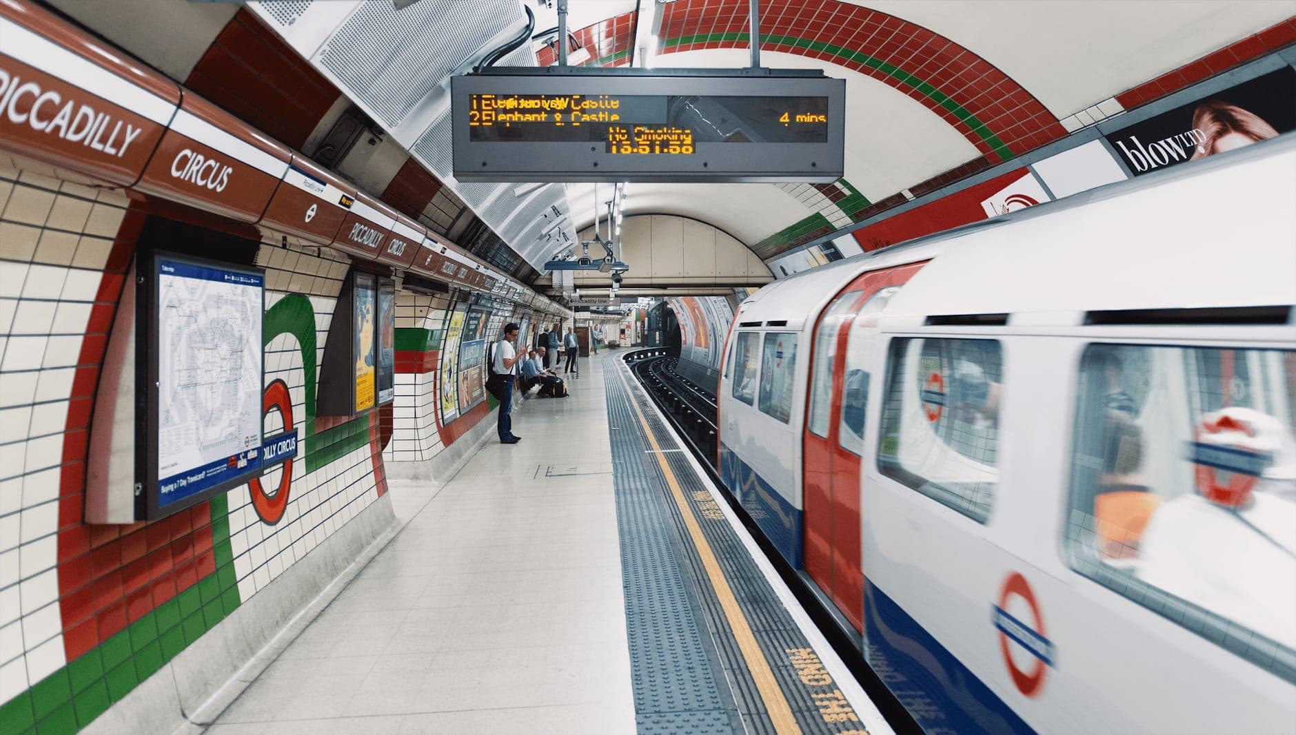 Piccadilly Circus'taki Londra metrosunun peronunda gelen bir tren ve bekleyen yolcular.