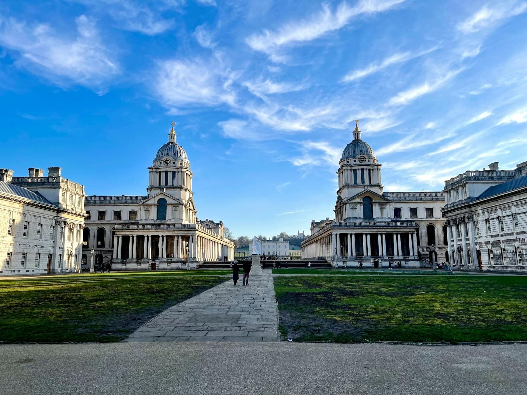 Londra'nın Greenwich semtindeki Old Royal Naval College'ın tarihi kubbeli binaları ve sütun dizilerinin mavi gökyüzü altında geniş açıdan görünümü.