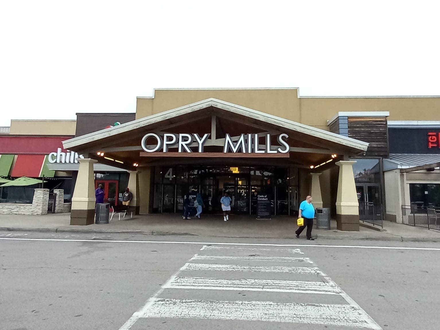 Haupteingang des Opry Mills Einkaufszentrums in Nashville mit großem Schild, überdachtem Eingangsbereich und vorbeigehenden Menschen an einem bewölkten Tag.