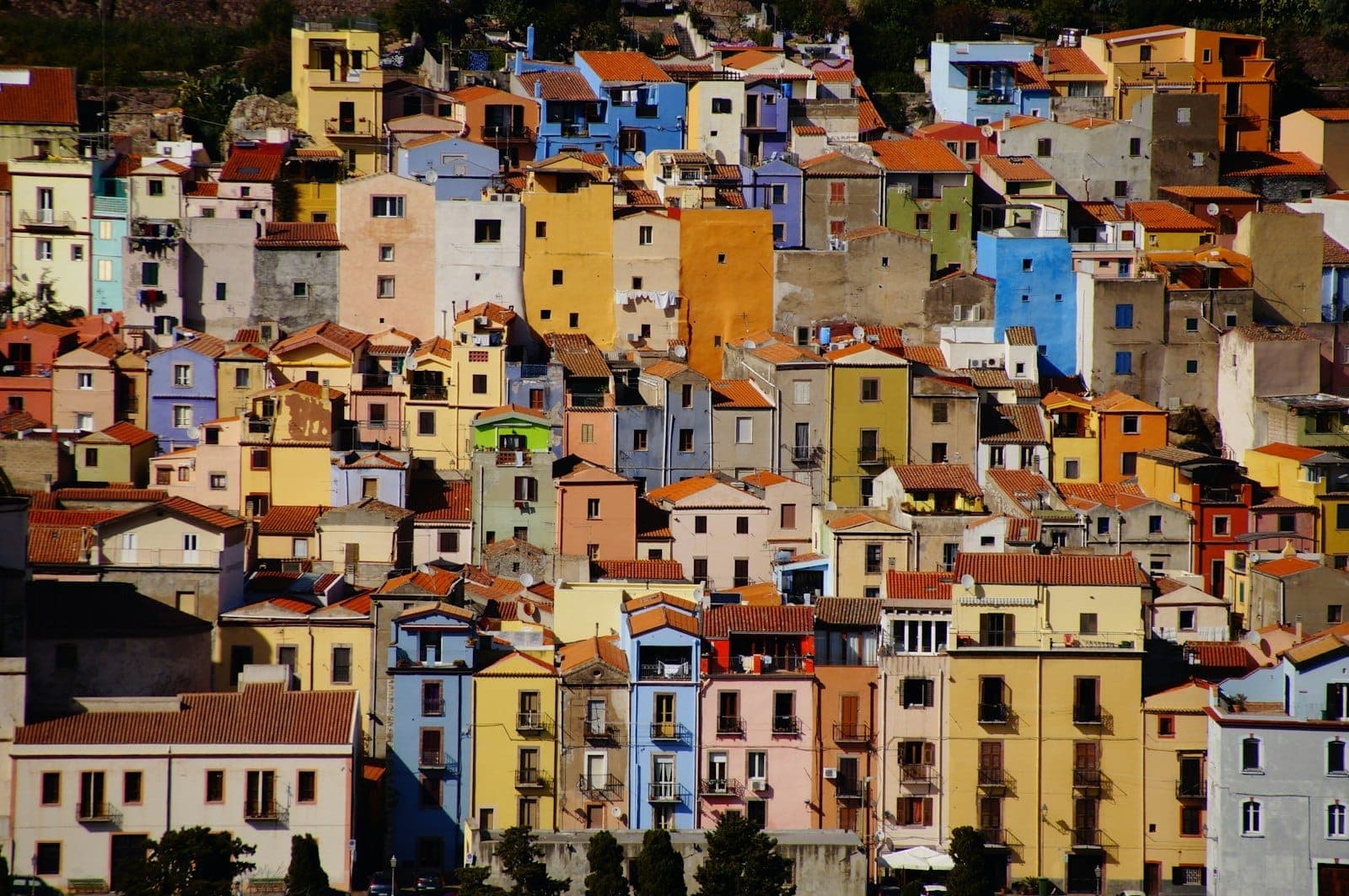 Coloridos edificios con tejados de terracota se agrupan en una colina en Oristano, creando una vista vibrante a la luz del día.