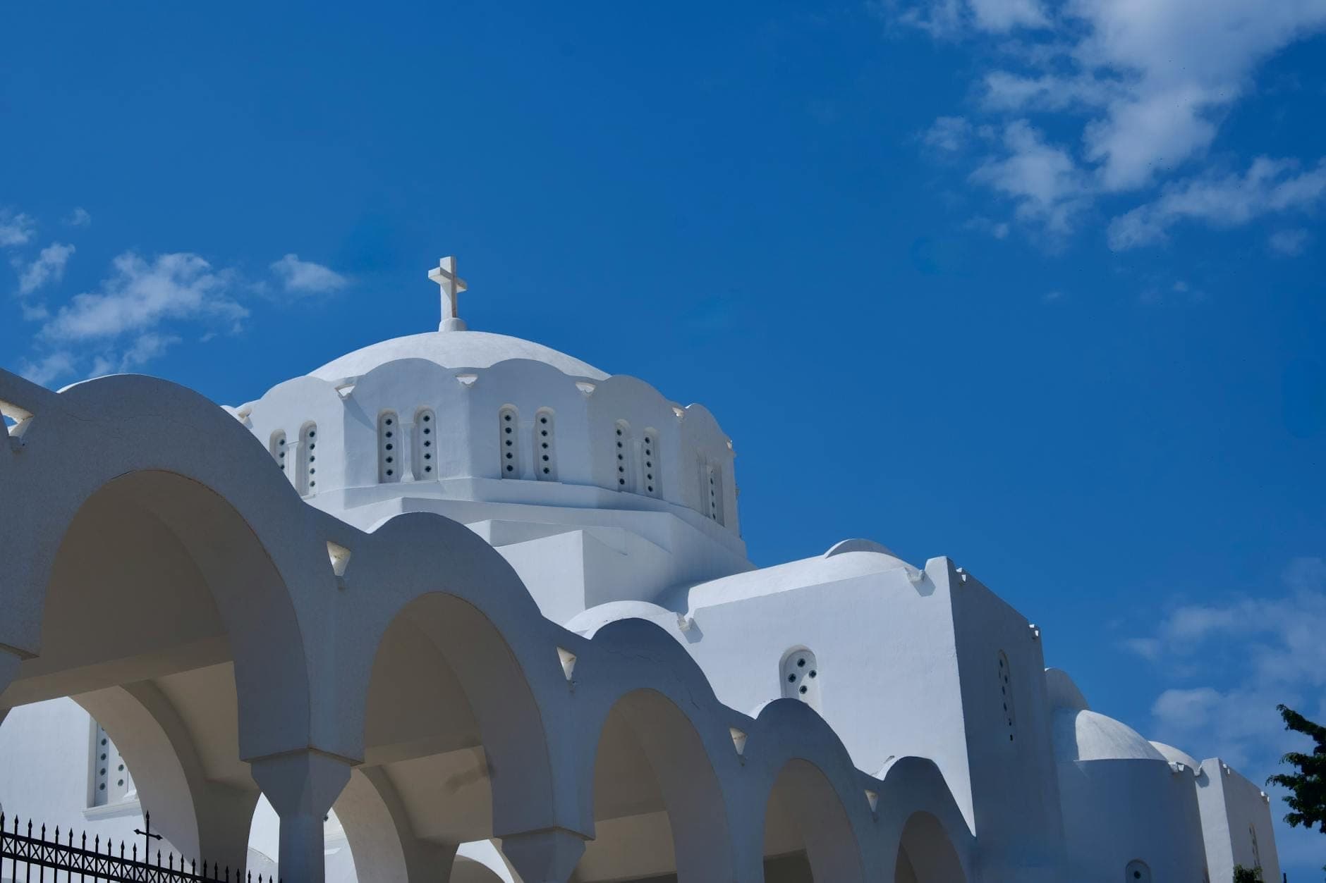 Weiß getünchte Orthodoxe Metropolitankathedrale in Fira mit markanter Bogenkolonnade und Kuppeldach unter strahlend blauem Himmel – ein Bild santorinischer Architektur.