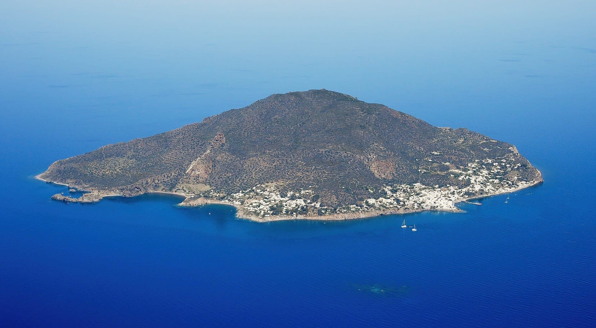 Pemandangan udara Pulau Panarea dengan medan vulkanik yang kasar, bangunan bercat putih, dan Laut Tyrrhenian biru dalam yang mengelilingi garis pantai.