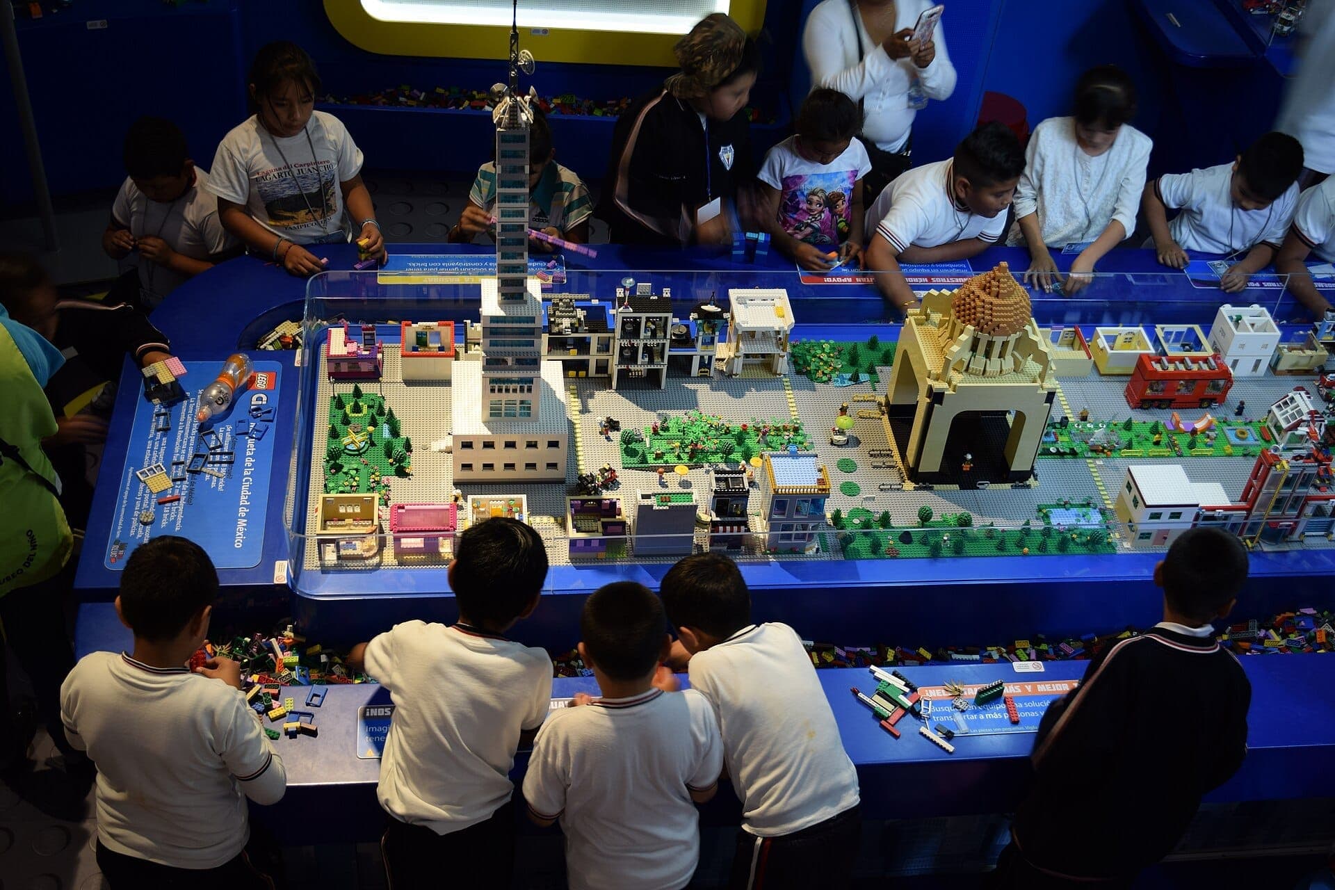 เด็กๆ โต้ตอบกับโมเดลเมือง LEGO ที่มีรายละเอียดที่ Papalote Museo del Niño โดยมีสถานที่สำคัญของ Ciudad de México ภายใต้แสงไฟภายในอาคารที่สว่างไสว