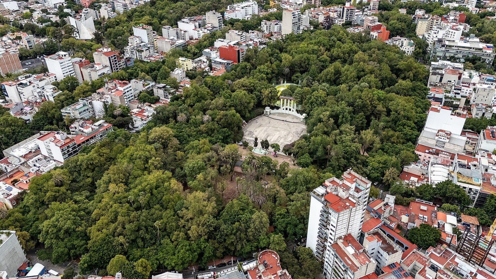 มุมมองทางอากาศของ Parque México ในย่าน Condesa เม็กซิโกซิตี้ แสดงให้เห็นต้นไม้สีเขียวขจีล้อมรอบด้วยอาคารในเมืองและฟอรัมกลางสไตล์ Art Deco