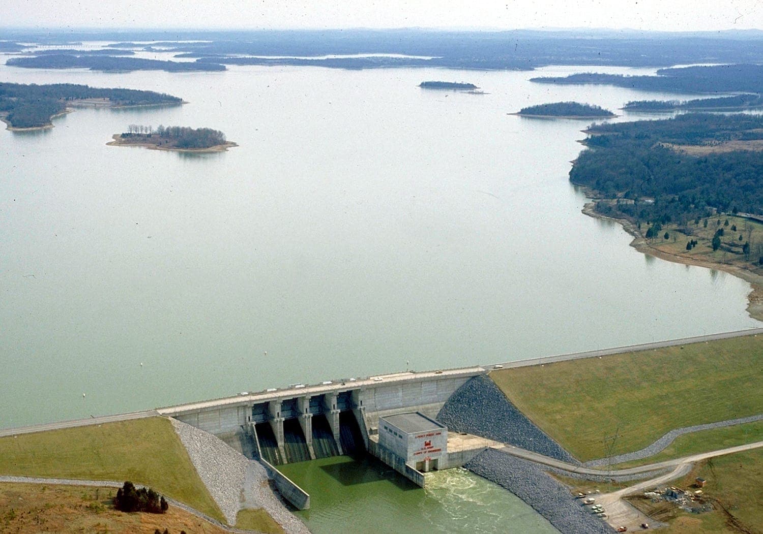 Aerial view of J. Percy Priest Lake showing the expansive reservoir, surrounding forested islands, and the concrete dam structure in the foreground.