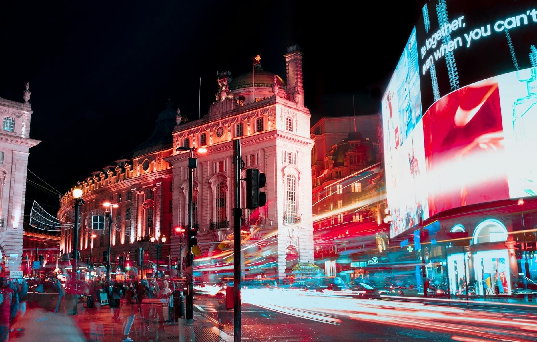 Piccadilly Circus bei Nacht mit leuchtenden Neonlichtern, beleuchteten Gebäuden, Lichtspuren des Verkehrs und Menschenmassen – das pulsierende Herz Londons.