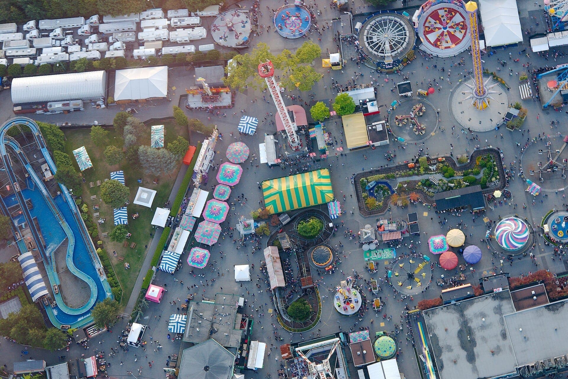 มุมมองทางอากาศของ Playland ที่ PNE ในเมือง Vancouver แสดงให้เห็นเครื่องเล่นสีสันสดใส เต็นท์งานรื่นเริง ทางน้ำไหล และฝูงชนในวันที่แดดสดใส